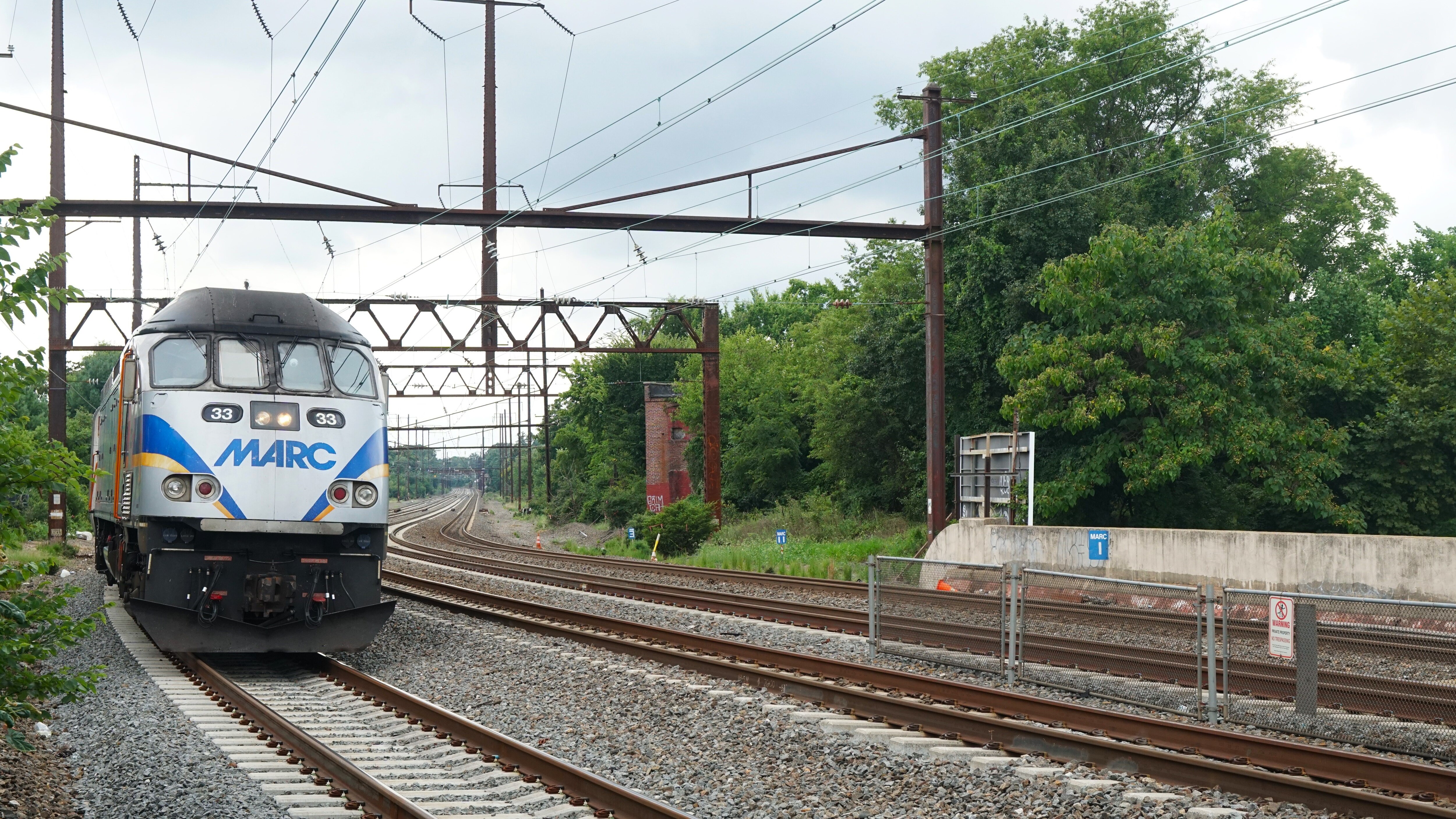 A silver train with the letters "MARC" on the front rolls into a station.