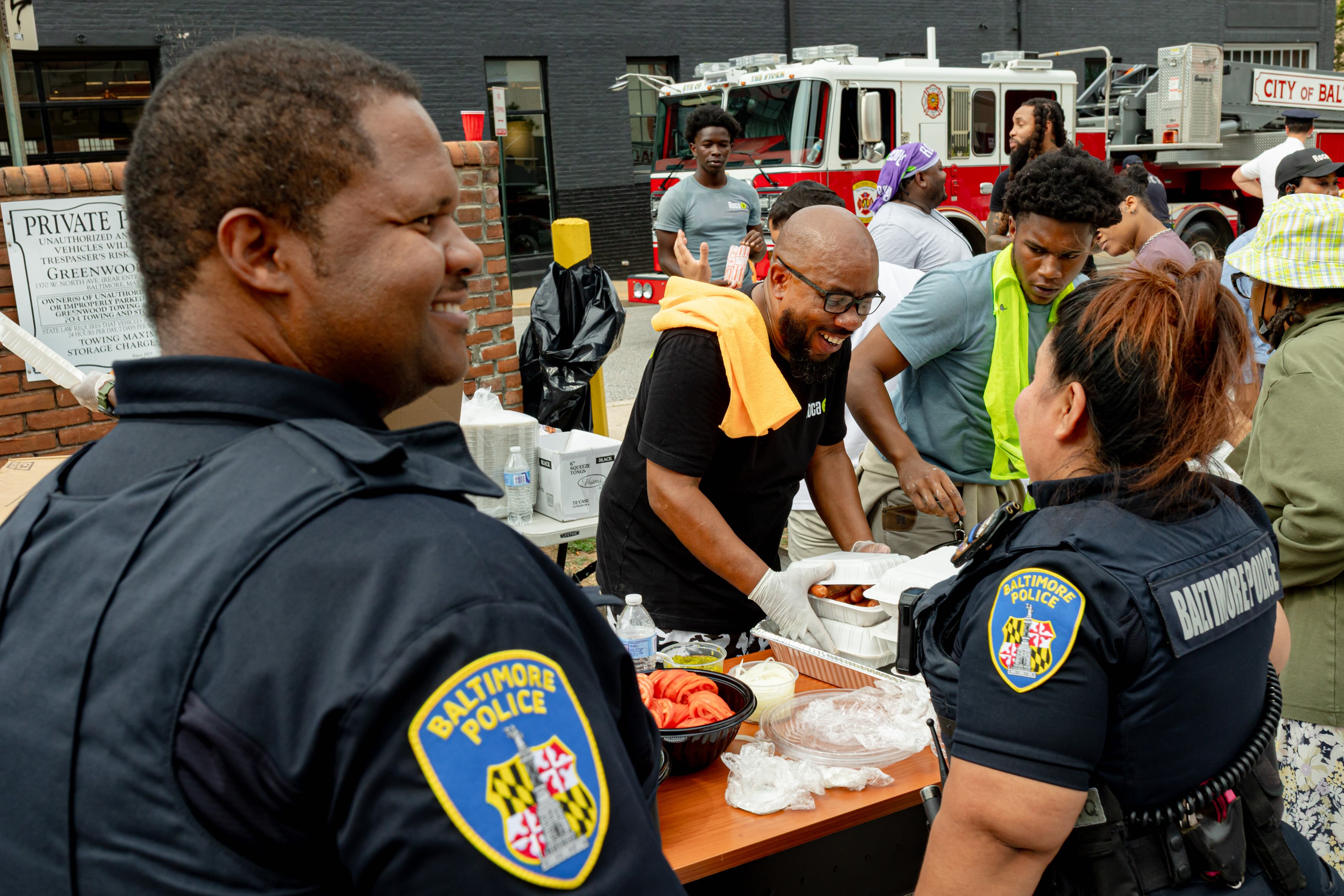 Roca youth worker John Young, center, and member Lamontae Royster serve hot dogs to Baltimore Police officers Dennis Gillespie and Stephanie Uruchima at Roca’s National Night Out cookout on August 5 outside the Waxter Center in Baltimore. 