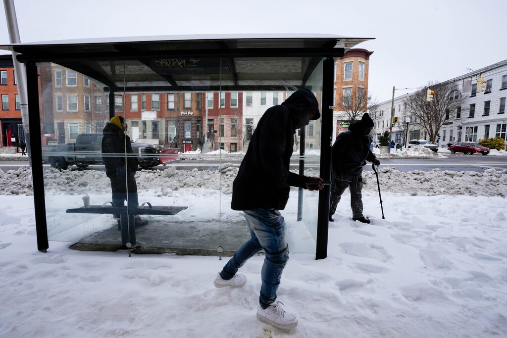 People wait near a bus shelter for the bus to arrive on 25th Street in the aftermath of a snowstorm in Baltimore, Md., on Wednesday, January 28, 2026.