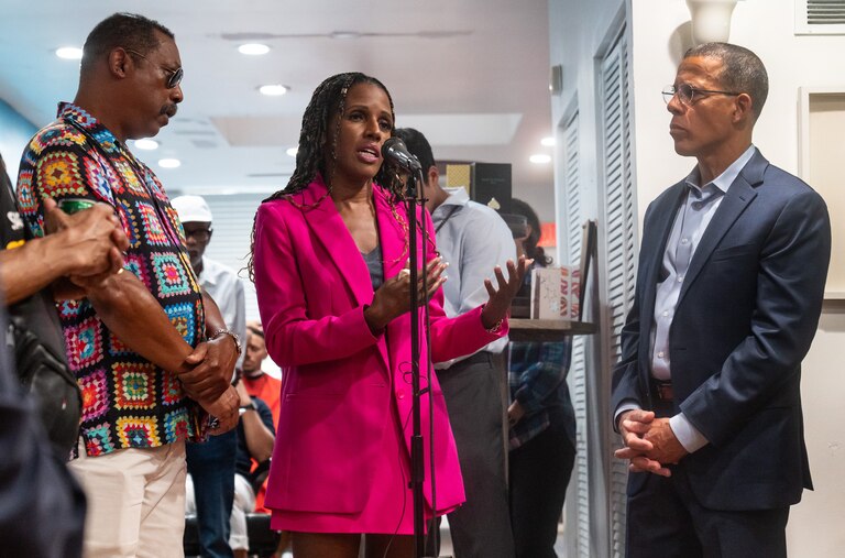 Natasha Dartigue, center, speaks at the mic. A community member, left, and Attorney General Anthony Brown listen.