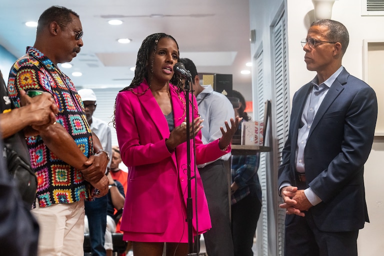Natasha Dartigue, center, speaks at the mic. A community member, left, and Attorney General Anthony Brown listen.