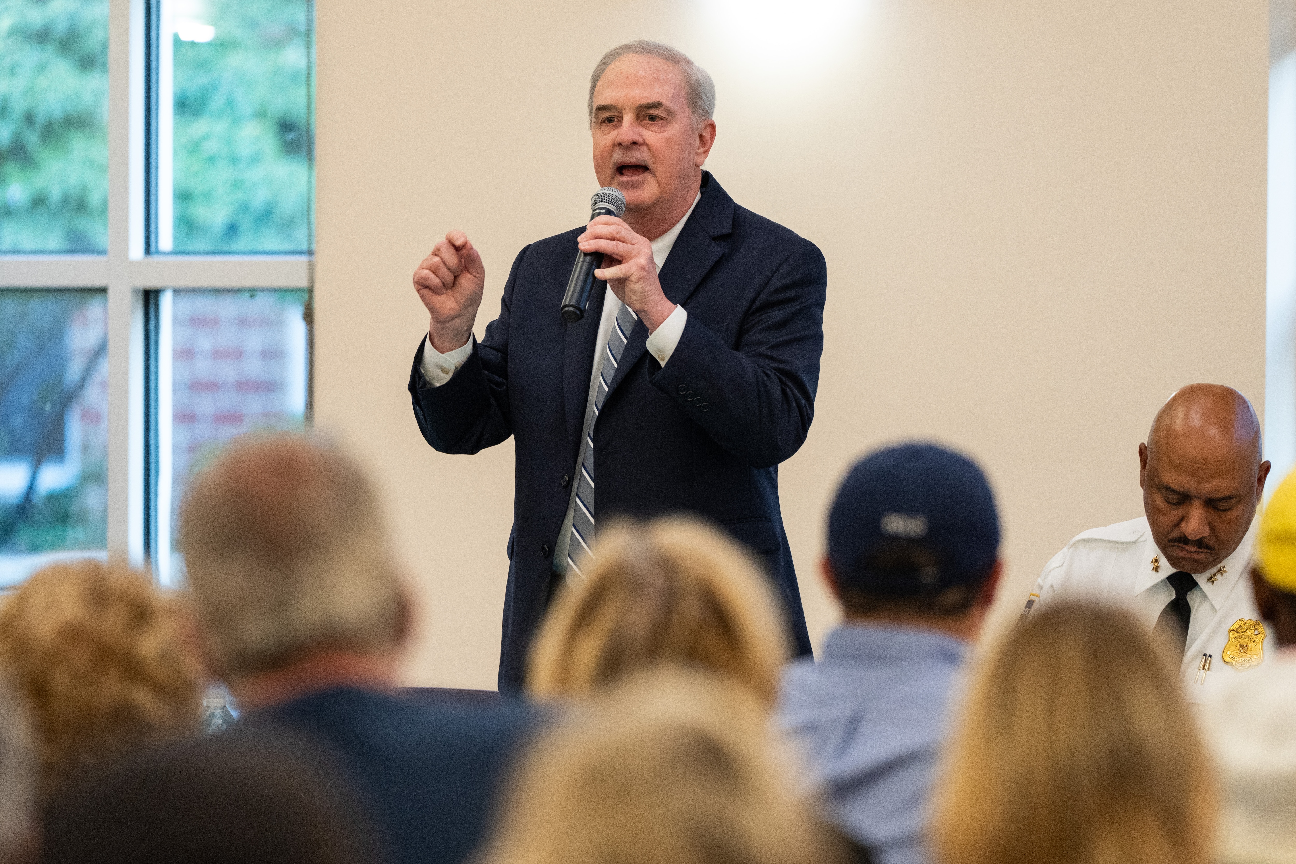 Scott Shellenberger speaks with his right hand lifted. The tops of the audience’s heads are seen at the bottom of the frame.