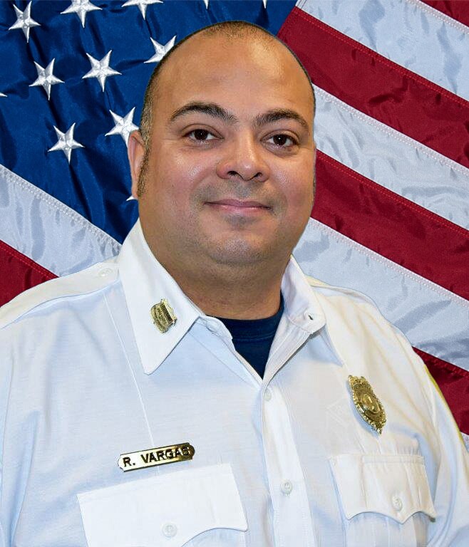 Lt. Raymond Vargas Jr. stands in front of an American flag