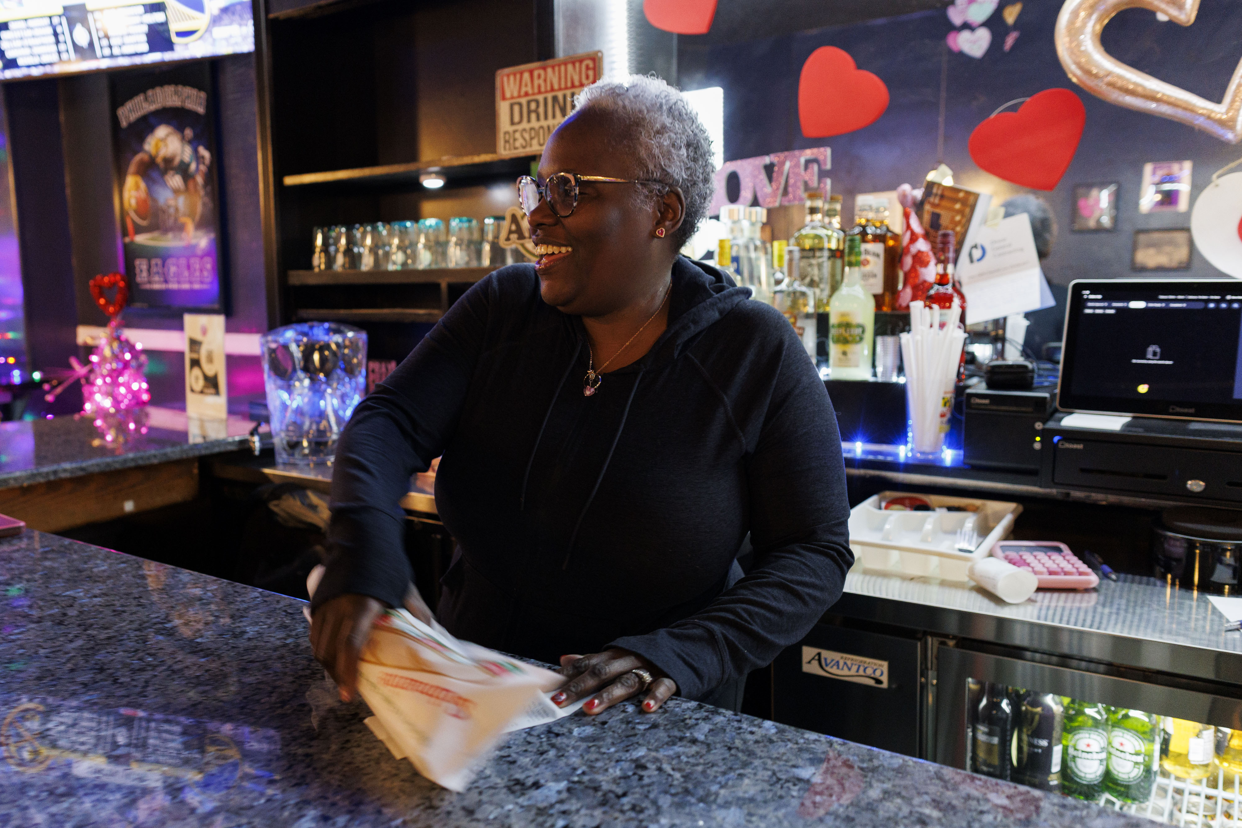 Mary Miles, owner of Dimples Bar and Grill in Locust Point, hands a customer a cheesesteak to go.