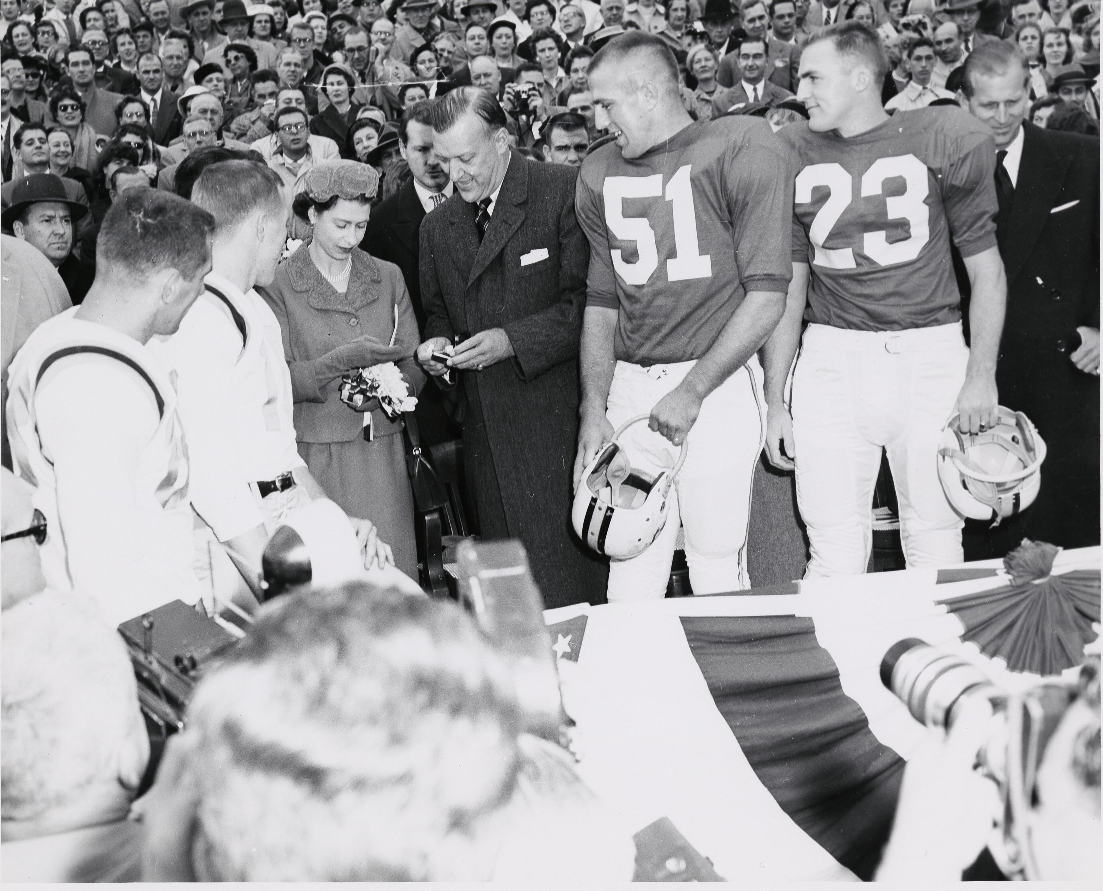Queen Elizabeth II with Governor Theodore McKeldin and team captains while checking the coin to be used for the coin toss at a University of Maryland football game against the University of North Carolina, October 19, 1957. Prince Philip is pictured at the far right. Courtesy of University of Maryland Archives.