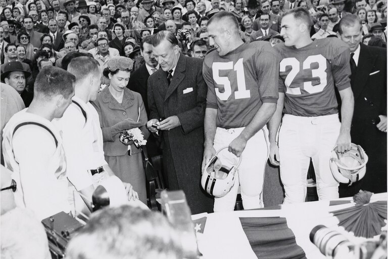 Queen Elizabeth II with Governor Theodore McKeldin and team captains while checking the coin to be used for the coin toss at a University of Maryland football game against the University of North Carolina, October 19, 1957. Prince Philip is pictured at the far right. Courtesy of University of Maryland Archives.
