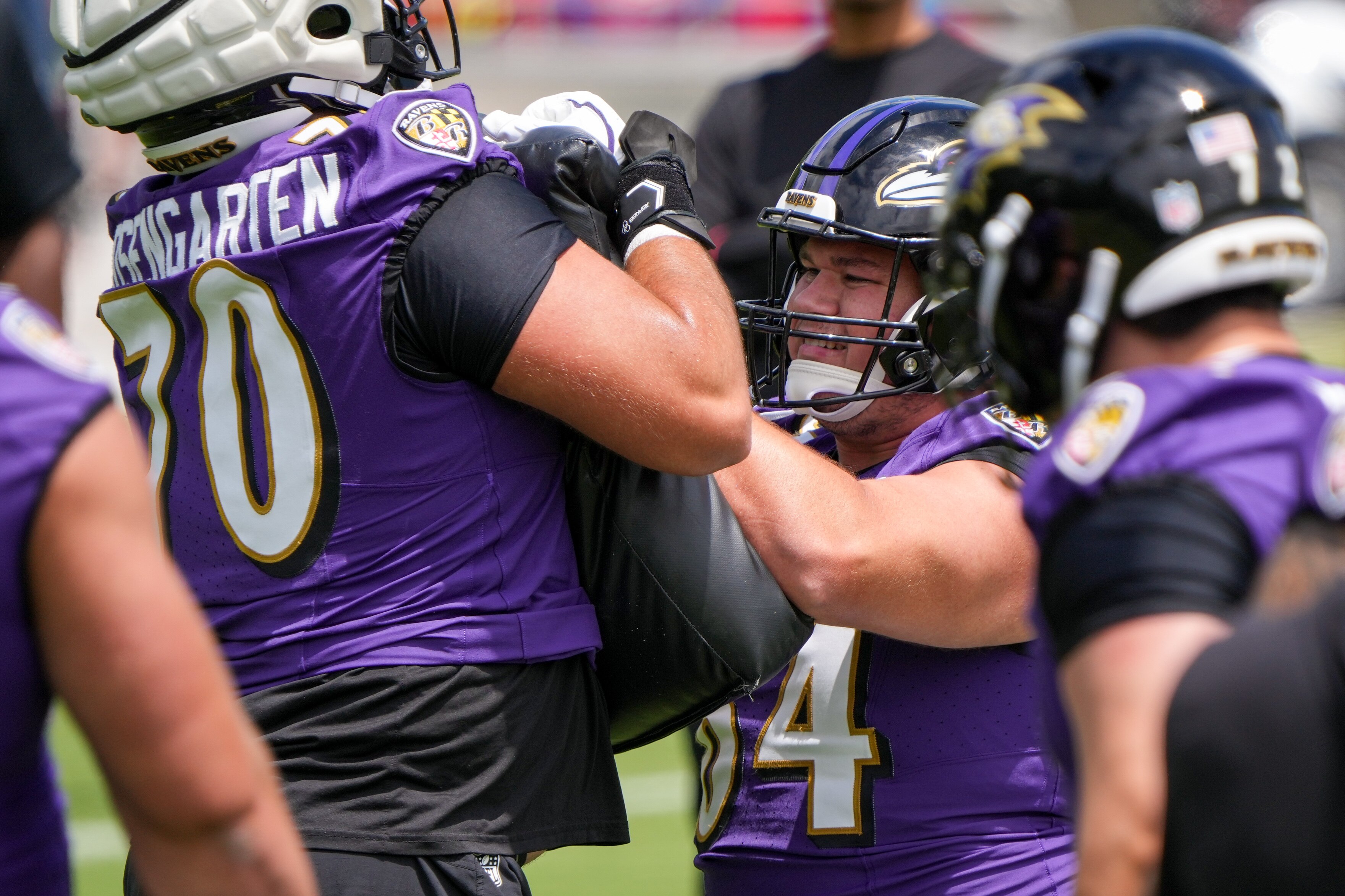 Tackle Roger Rosengarten (70) assists center Tyler Linderbaum (64) with a drill during the Baltimore Ravens’ first mandatory minicamp of the year at the Under Armour Performance Center in Owings Mills on June 11, 2024.