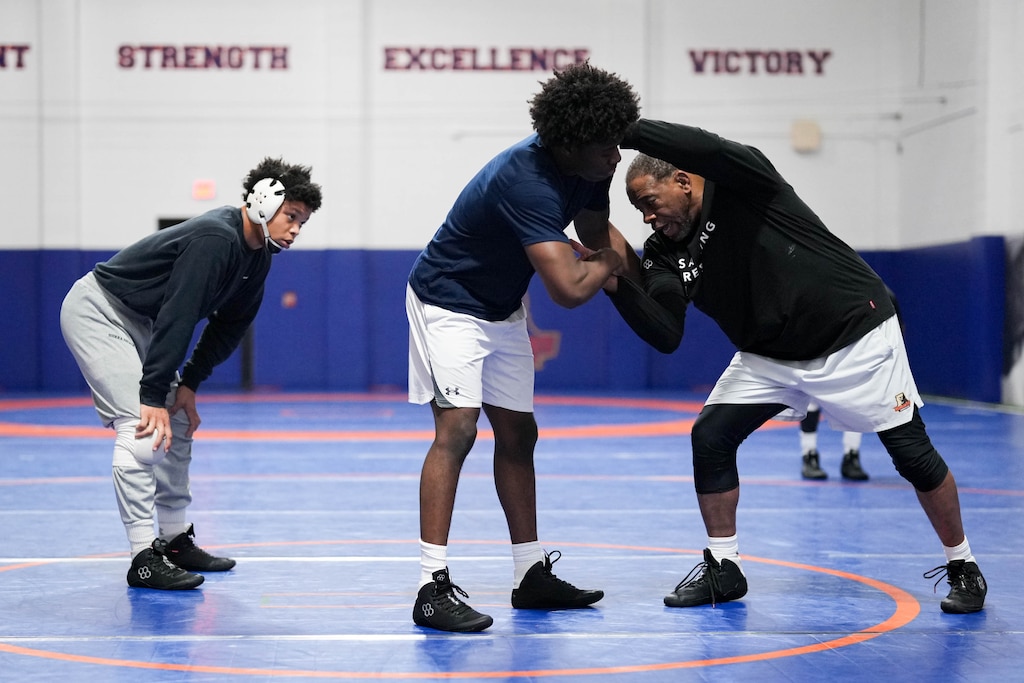 Yannis Charles listens as his coach, Kenny Monday, right, does a demonstration with student Aaron Turner during wrestling practice at Hill Field House on Morgan State University’s campus in Baltimore, Md., on Monday, March 16, 2026.