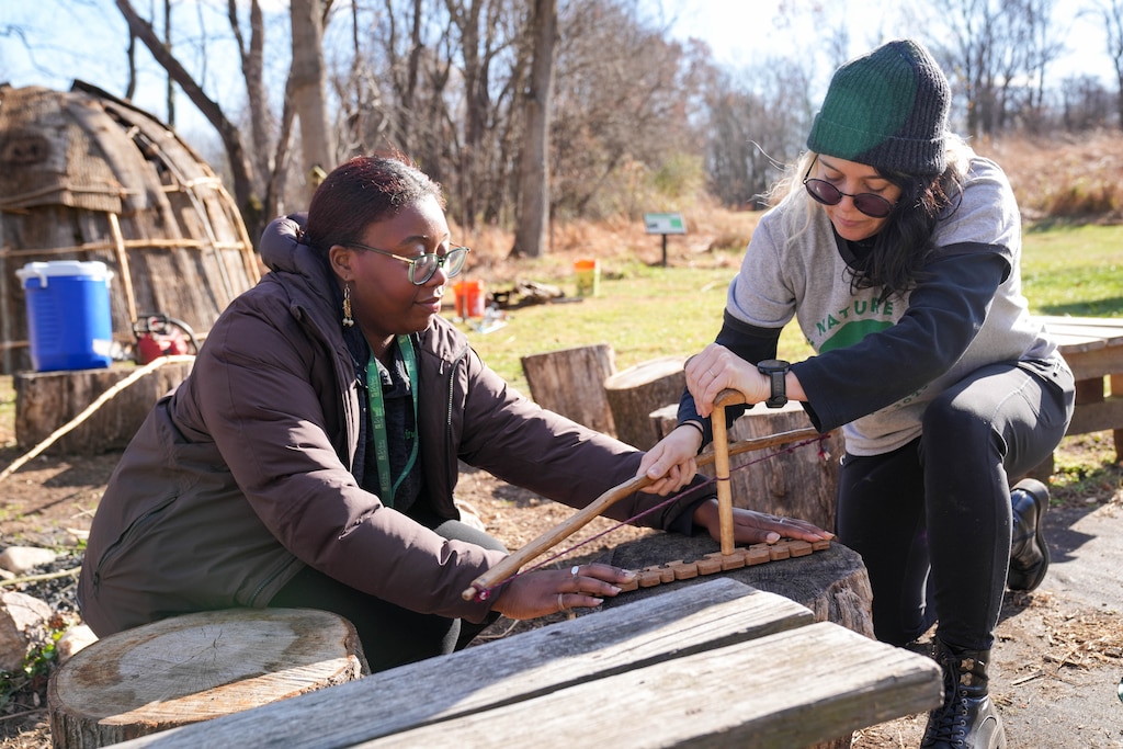 Genevieve Green, digital content creator, left, assists Brittany Rogers, manager of school programs, at the fire-making station at the Irvine Nature Center’s Native American Educational Site in Owings Mills, Md., on Thursday, November 13, 2025. The Center will host a free Indigenous Peoples Celebration on Sunday, November 23.