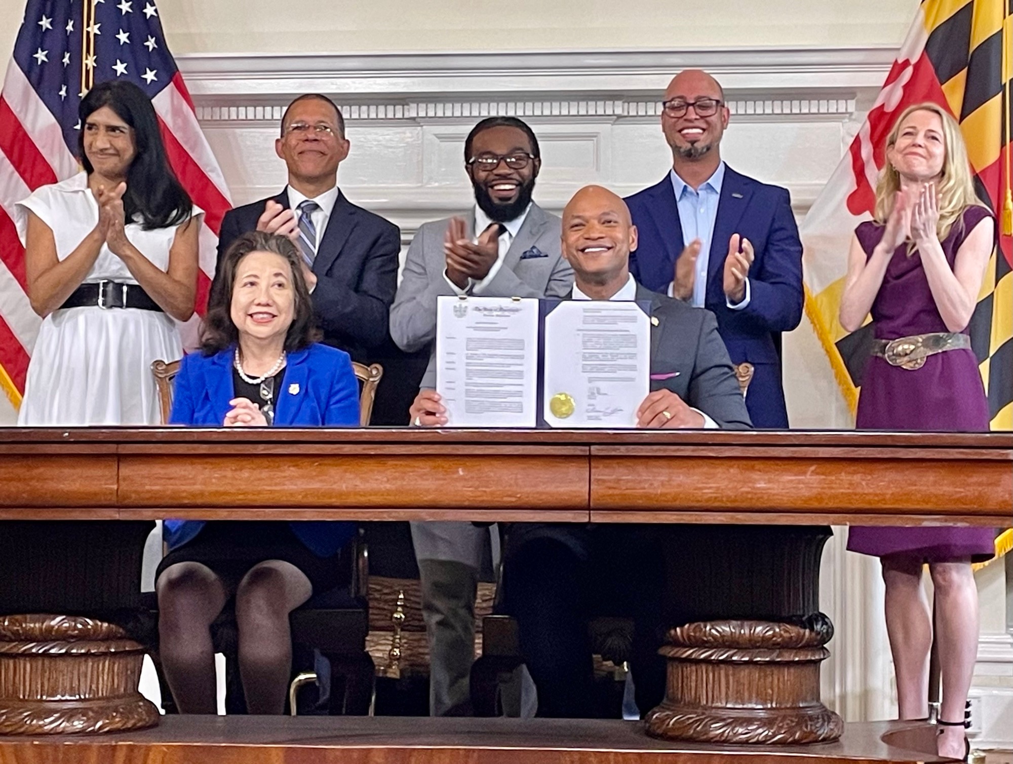 Maryland Gov. Wes Moore holds up paperwork pardoning more than 175,000 cannabis-related convictions during a ceremony at the State House in Annapolis on Monday, June 17, 2024.. Alongside him is Secretary of State Susan Lee, and standing, from left, are: Lt. Gov. Aruna Miller; Attorney General Anthony Brown; Shiloh Jordan, who will have a charge pardoned; Jason Ortiz of the Last Prisoner Project; and Heather Warnken, executive director of the Center for Criminal Justice Reform at the University of Baltimore. (Brenda Wintrode / The Baltimore Banner)
