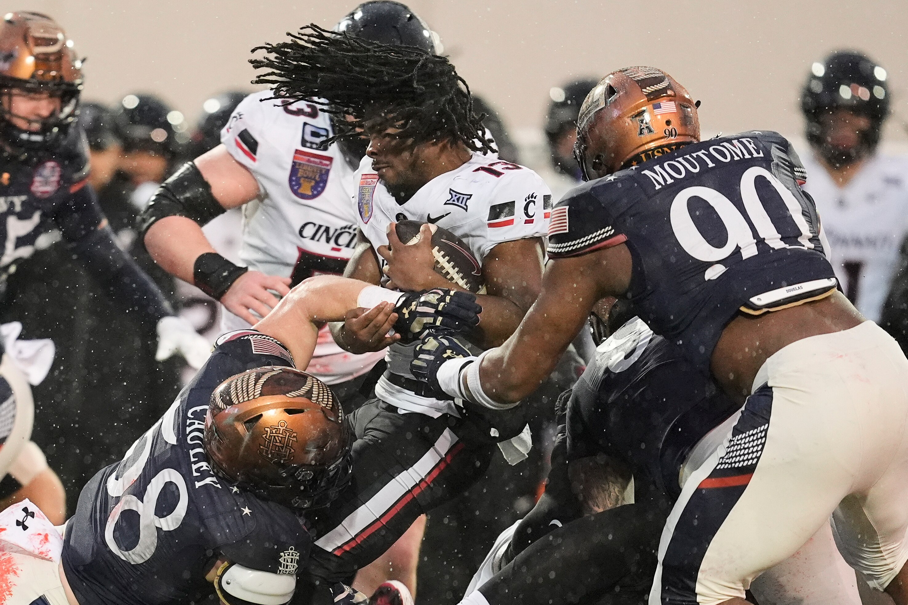 Cincinnati running back Zion Johnson loses his helmet as he tackled by Navy linebacker Coleman Cauley and defensive end Julien Moutome during the first quarter of the Liberty Bowl.