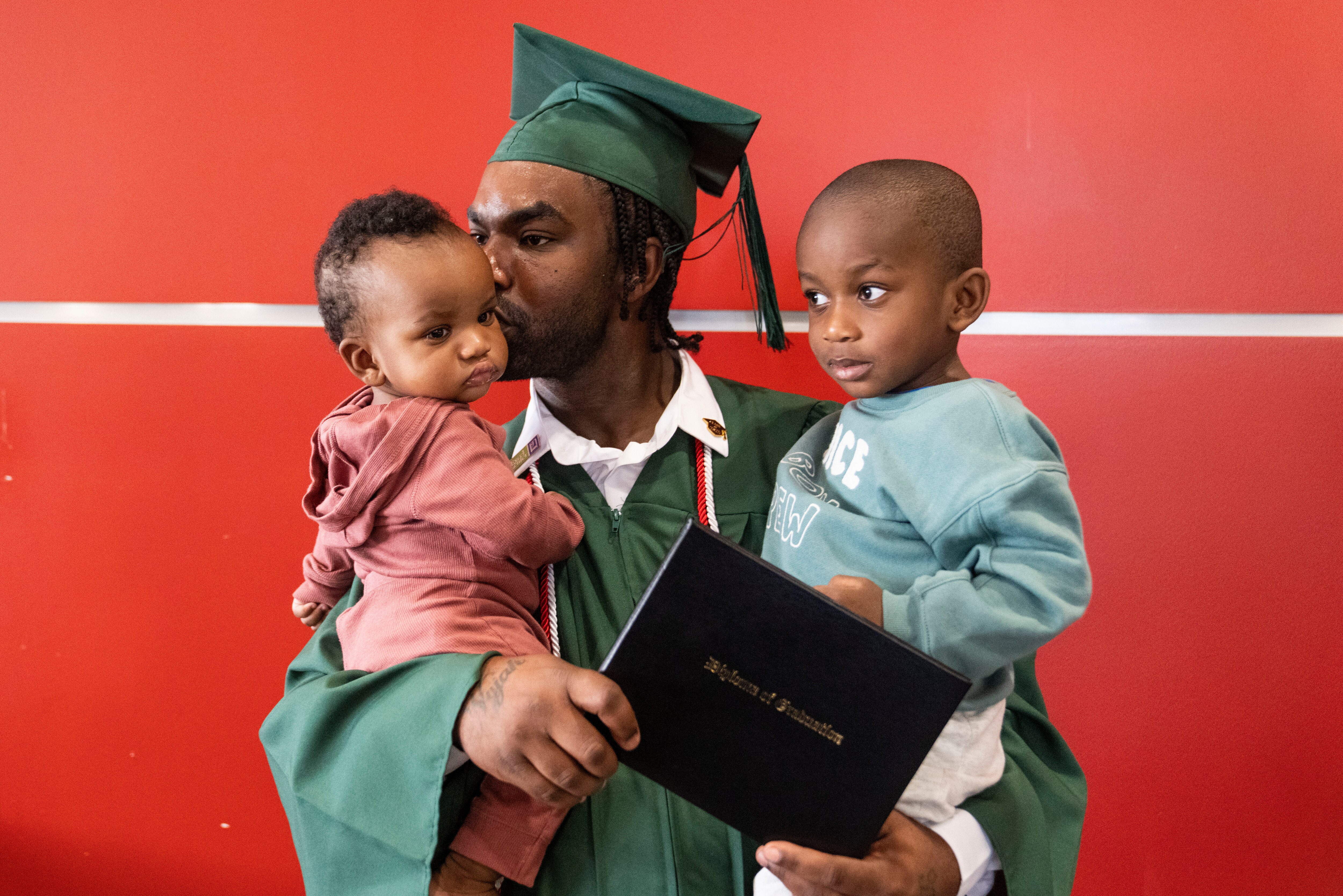 Antonio Pennix holding his son Avion Pennix and Avi Pennix for a portrait after his commencement ceremony at the University of Maryland, Baltimore, on Friday, September 19, 2025. Pennix was among 50 graduates from the Excel Center — a free high school for adult learners in Maryland — there to receive their diplomas.