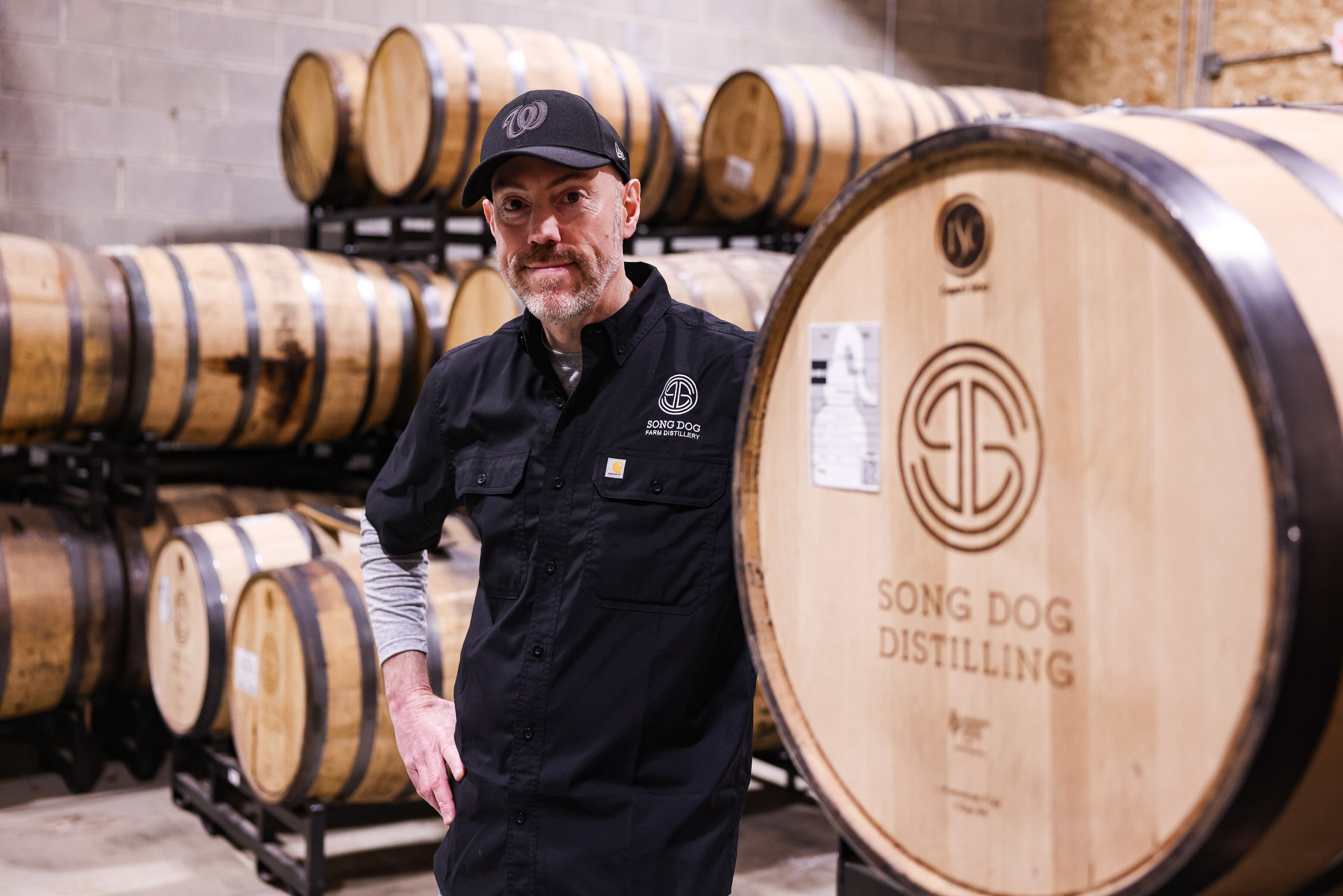 David Harris, who opened Song Dog Farm Distillery with his wife in Boyds, stands with barrels used for aging bourbon and rye whiskey.