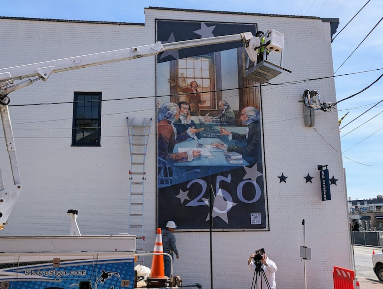 An installation crew hangs a mural on a downtown Annapolis building depicting Revolutionary-era lawmakers working in Annapolis.