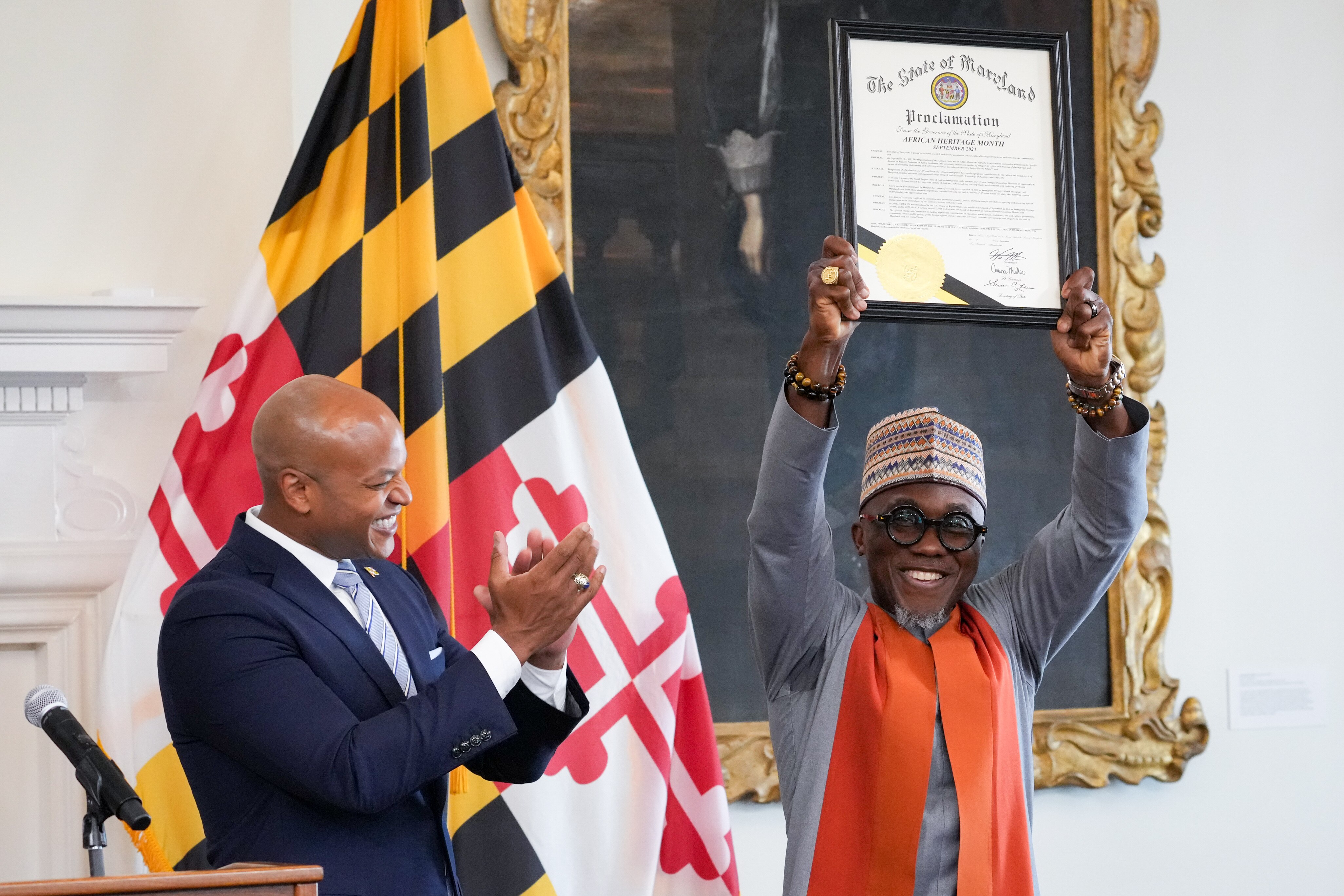 Gov. Wes Moore applauds as Chukwunonso “Vincent” Iweanoge, chair of the Governor’s Commission on African Affairs, raises the official proclamation to name September as African Heritage Month.