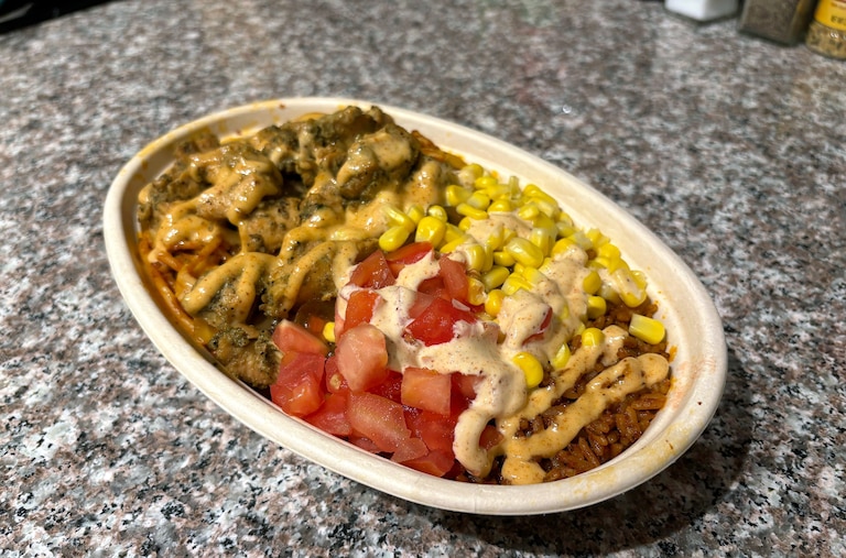 A bowl of half jollof rice, half jollof noodles, grilled chicken, yassa onions, corn, fresh tomato and suya aioli from Jollof Bowl in Cross Street Market.