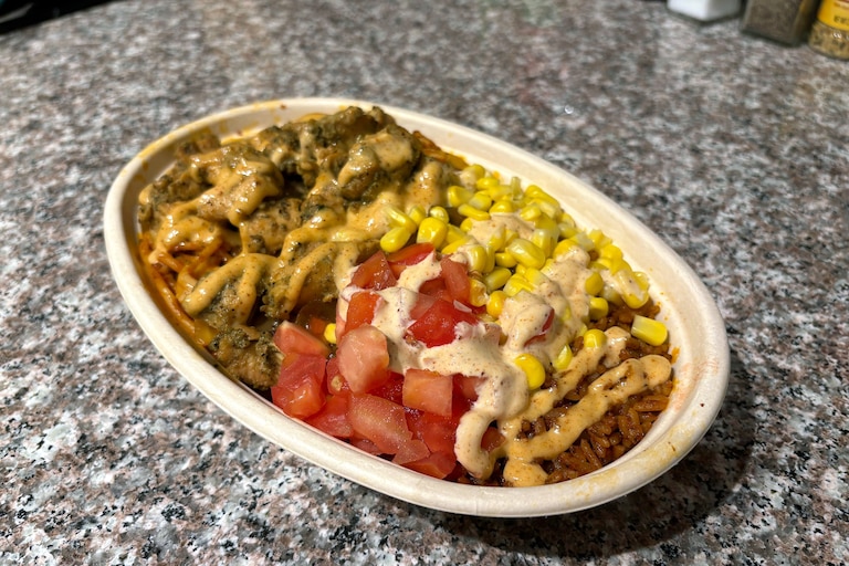 A bowl of half jollof rice, half jollof noodles, grilled chicken, yassa onions, corn, fresh tomato and suya aioli from Jollof Bowl in Cross Street Market.