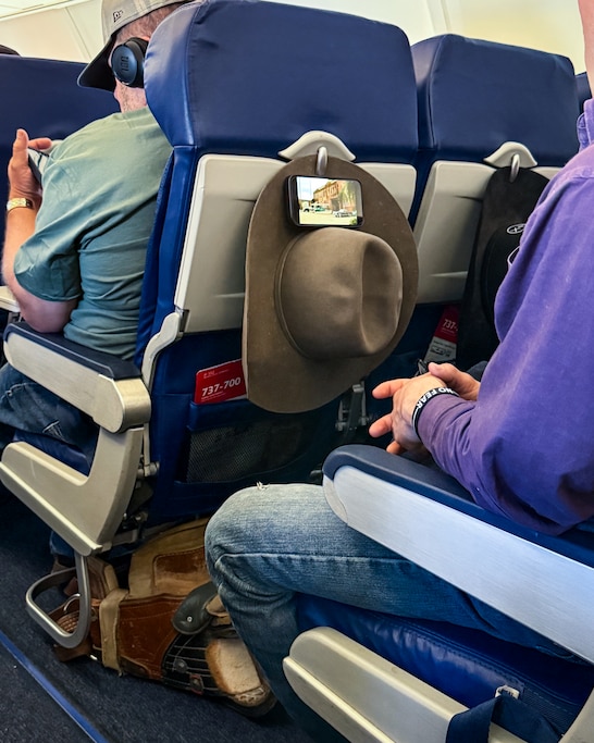 A passenger uses their cowboy hat as a way to prop their phone up on the flight.