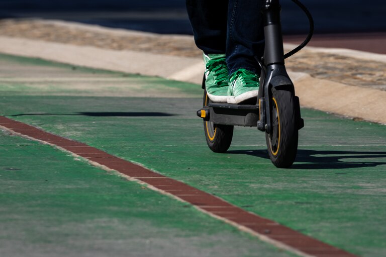 A close-up of someone's green shoes as they ride a scooter on the green pedestrian/biker/scooter section of the road.