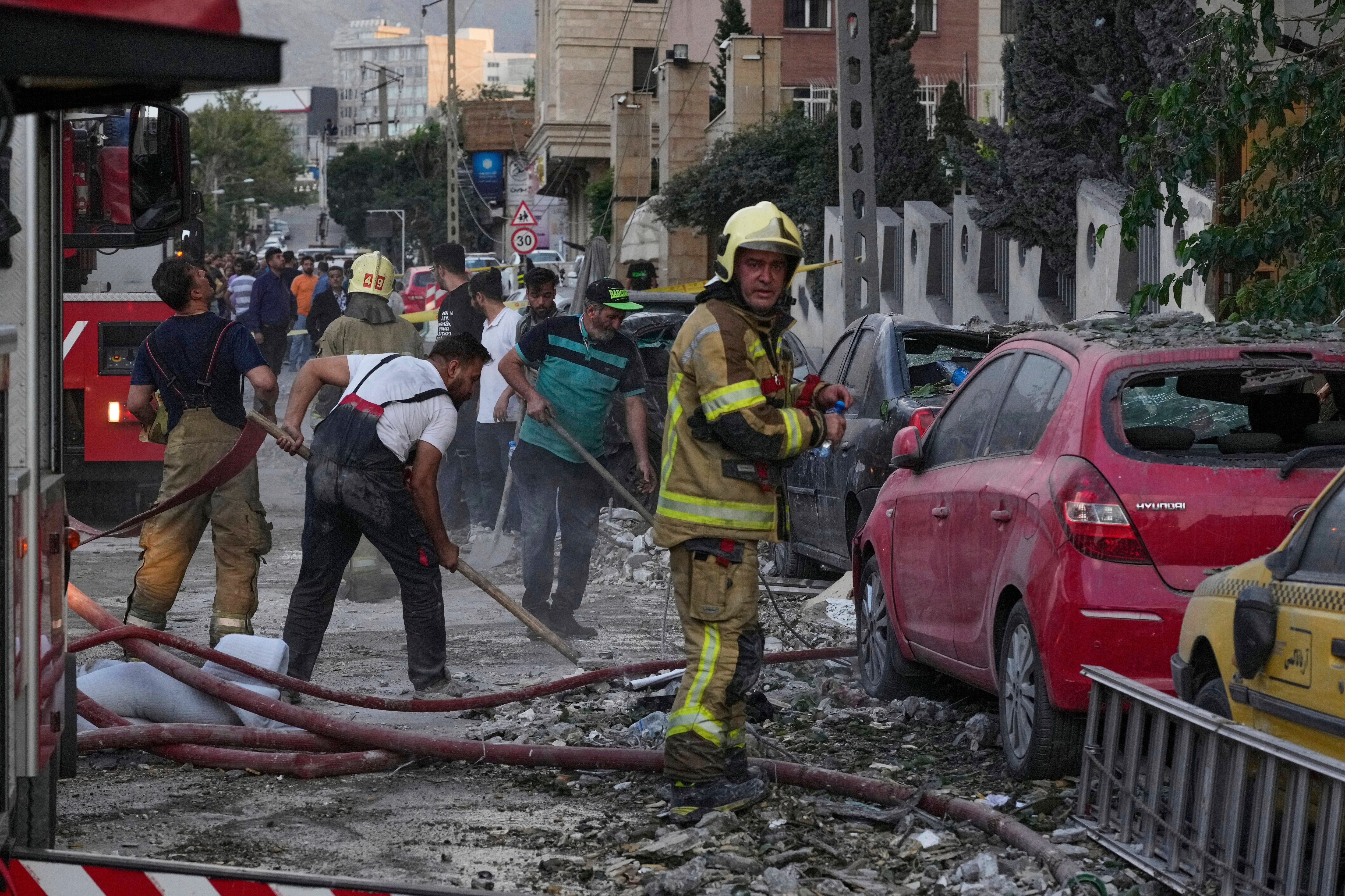 Firefighters and people clean up the scene of an explosion at a residence compound after Israeli attacks in Tehran, Friday, June 13, 2025. (AP Photo/Vahid Salemi)