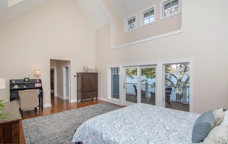 a bedroom with light beige walls, high ceilings and a bed with a blue and white bedspread.
