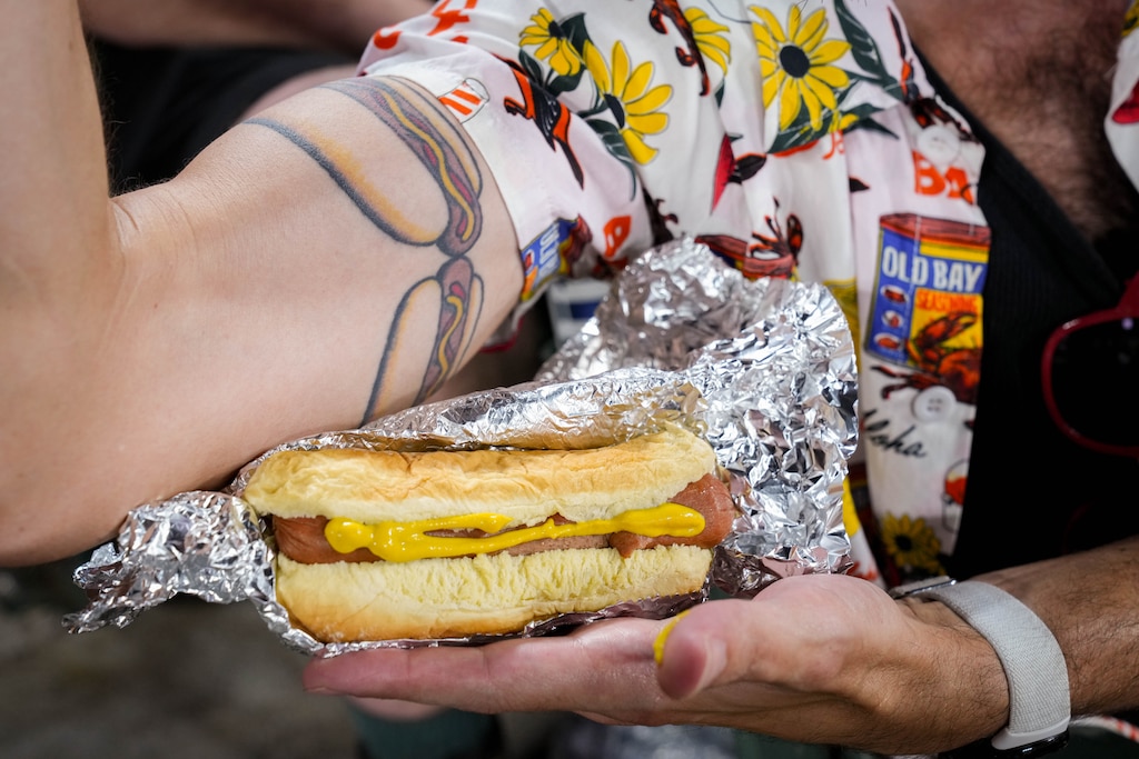 Craig Chilcott displays his hot dog tattoo as he holds a hot dog during a baseball game between the Baltimore Orioles and the Cleveland Guardians at Oriole Park at Camden Yards in Baltimore, Md. on Wednesday, September 9, 2026. Chilcott, along with Casey Jarvis, owner of Glizzy’s Wagyu Dogs, and other friends in their section brought hundreds of hot dogs with them to complete the 9 9 9 challenge during the game Thursday night.