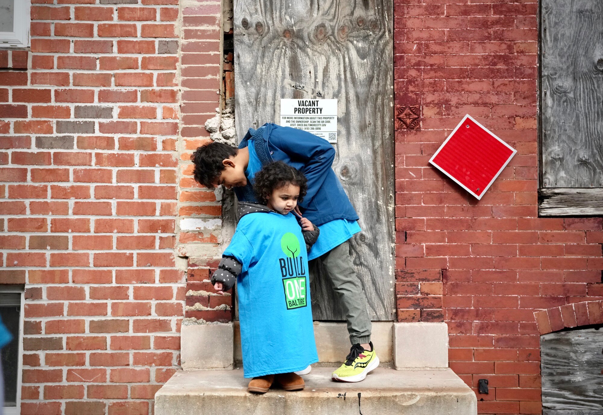Eliana Wharton and brother Christopher Wharton play outside of a vacant home on West Saratoga street during a press conference hosted by Build One Baltimore on February 16, 2023.
