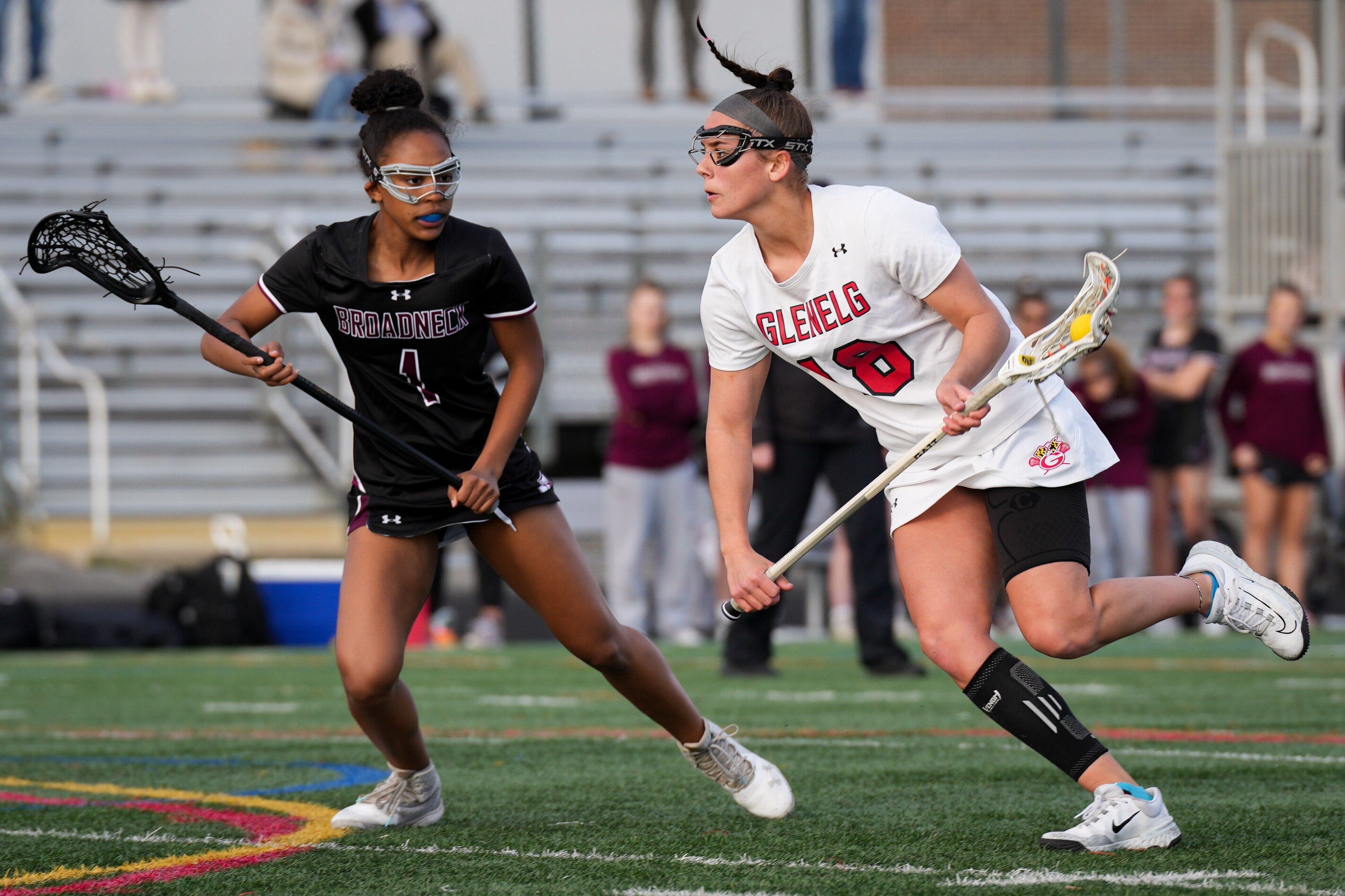 Glenelg’s Isa Torres (18) runs past Broadneck’s Nya Williams (1)  in the first half of a girls lacrosse game at Glenelg High School on Tuesday, March 28. Glenelg defeated Broadneck, 11-8.
