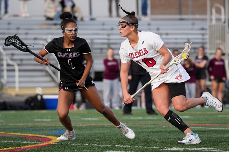 Glenelg’s Isa Torres (18) runs past Broadneck’s Nya Williams (1) in the first half of a girls lacrosse game at Glenelg High School on Tuesday, March 28. Glenelg defeated Broadneck, 11-8.