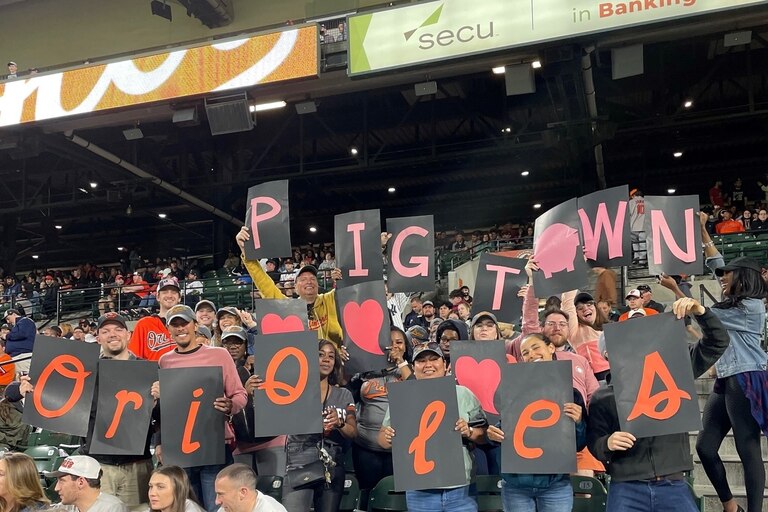 A Citizens of Pigtown group at Camden Yards, posing in the stands with signage that spells out "Pigtown hearts Orioles." Citizens of Pigtown is a neighborhood association that represents residents and businesses.