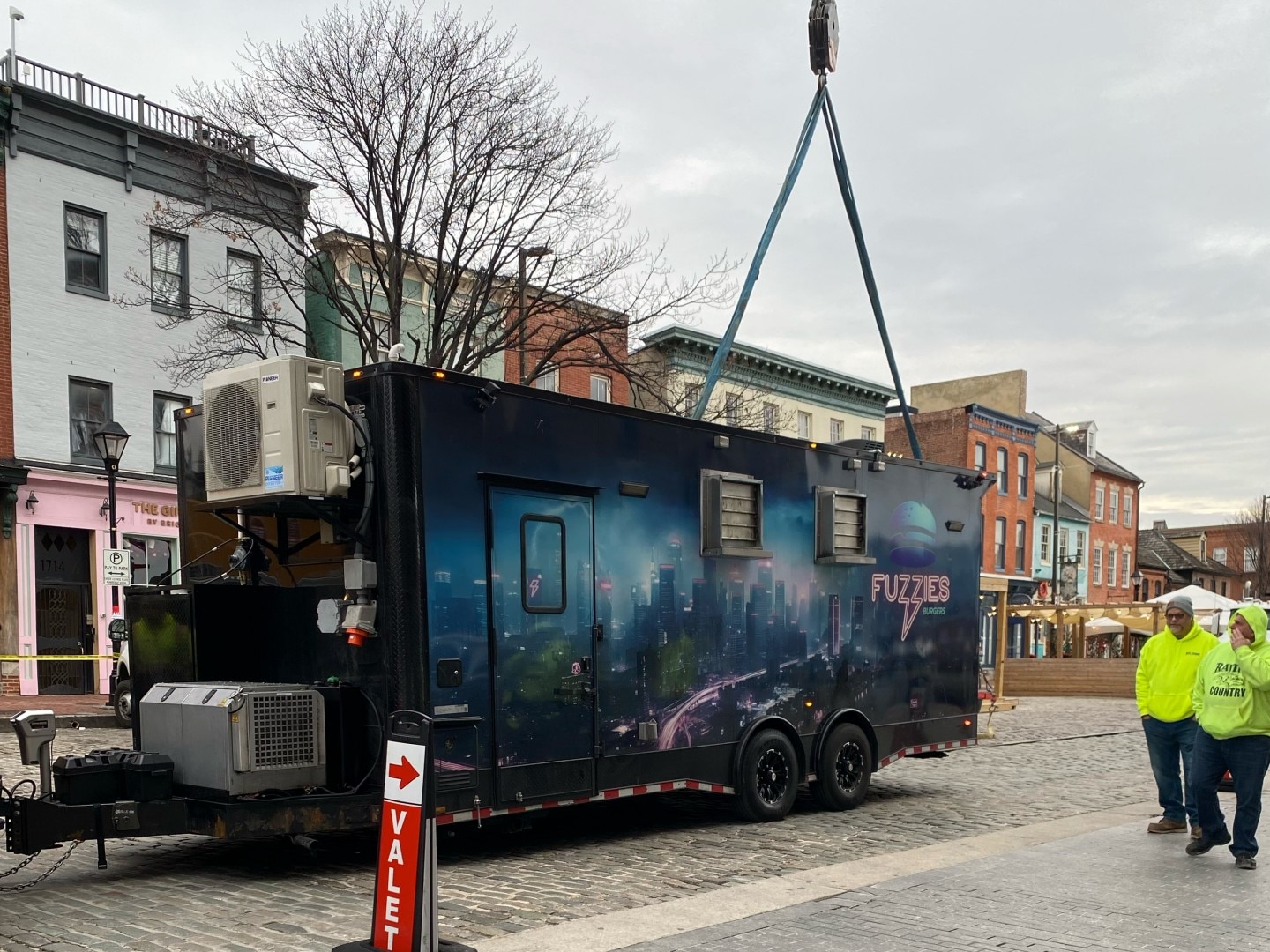 Fuzzies food trailer is fastened to a crane so that it can be lifted into the courtyard of The Undefeated, a new bar in Fells Point.