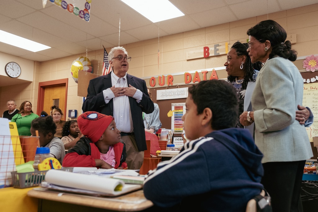 Montgomery Education Association President David Stein (left) recognizes second grade teacher Estelle Moore (right) inside her classroom at Greencastle Elementary School while National Education Association President Becky Pringle embraces her. Moore was surprised by school officials, former students, education leadership, and family at a morning assembly with students who had gathered to recognize her 55 years in education.