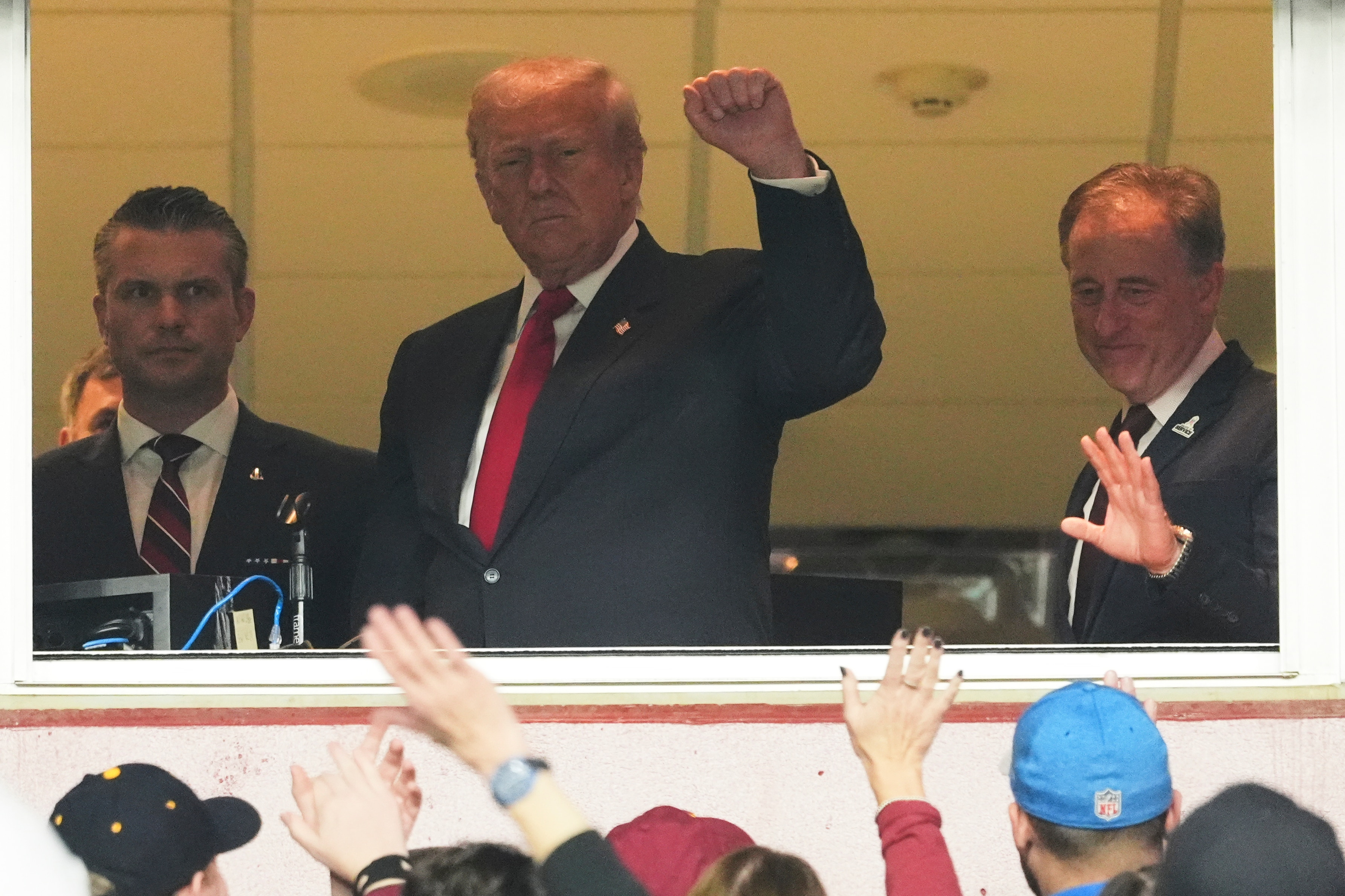 President Donald Trump, center, gestures to the crowd alongside Defense Secretary Pete Hegseth, left, and Washington Commanders owner Josh Harris, as they attend an NFL football game between the Commanders and the Detroit Lions at Northwest Stadium in Landover, Md., Sunday, Nov. 9, 2025.