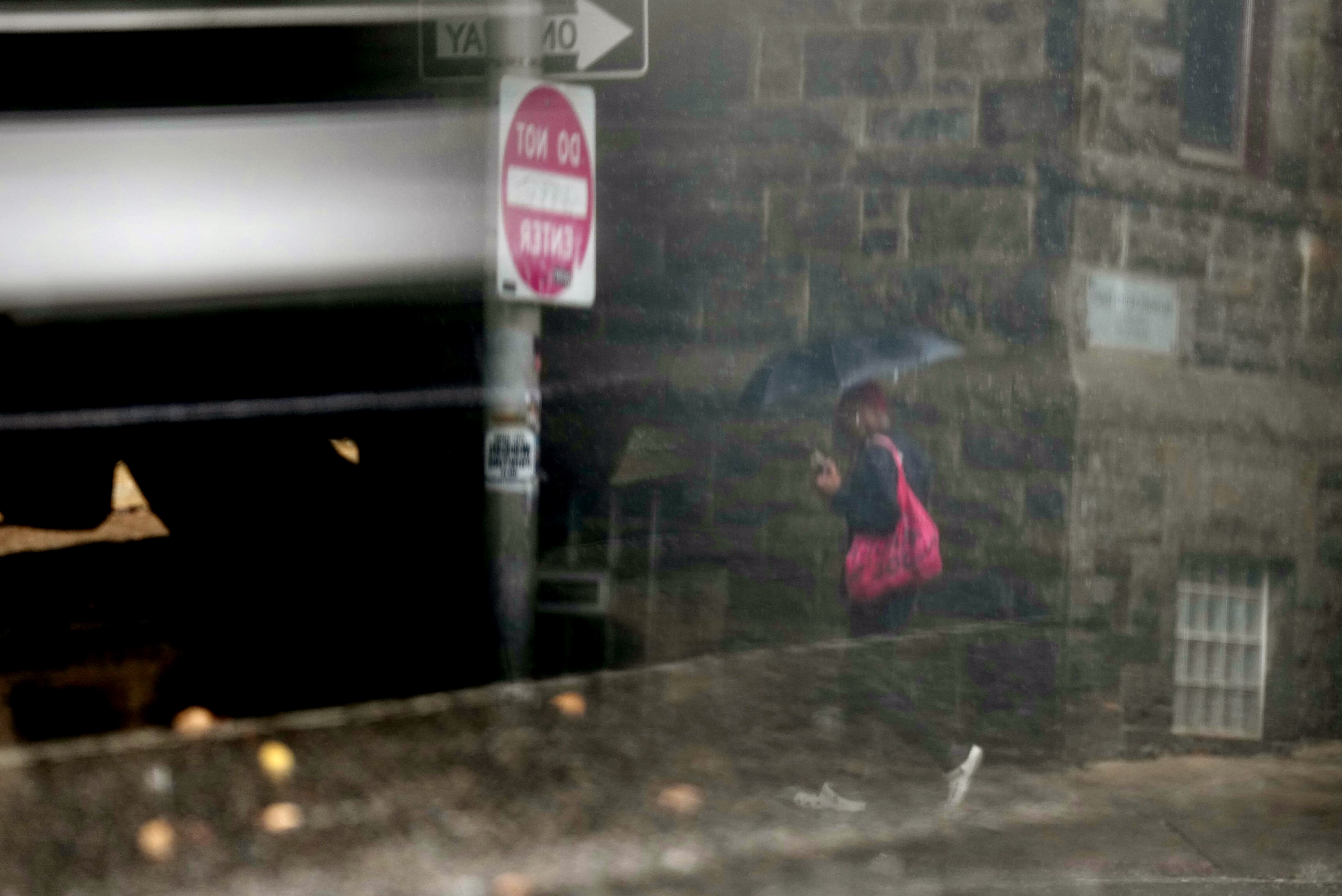 Seen reflected in a car mirror, a woman crosses St. Paul Street in Baltimore with an umbrella during a thunderstorm on Thursday, August 14, 2025.