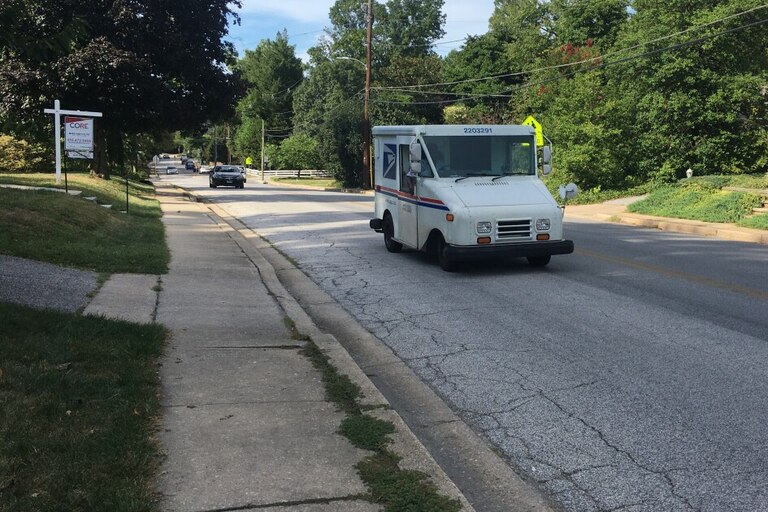 A mail truck drives down Bellona Avenue in Baltimore County. A number of cracks are visible in the road. John Lee/WYPR.