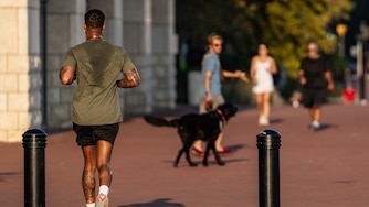 A man running away from the camera's t-shirt is drenched with sweat.
