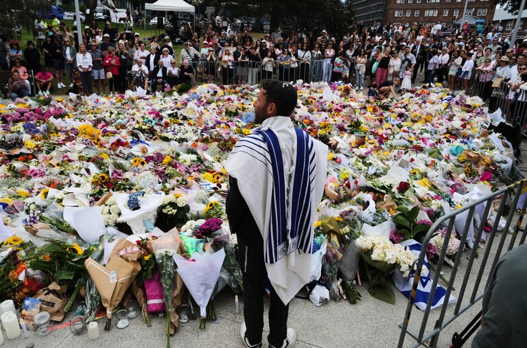 Rabbi Yossi Friedman speaks to people gathering at a flower memorial by the Bondi Pavilion at Bondi Beach on Tuesday, Dec. 16, 2025, following Sunday's shooting in Sydney, Australia. (AP Photo/Mark Baker)