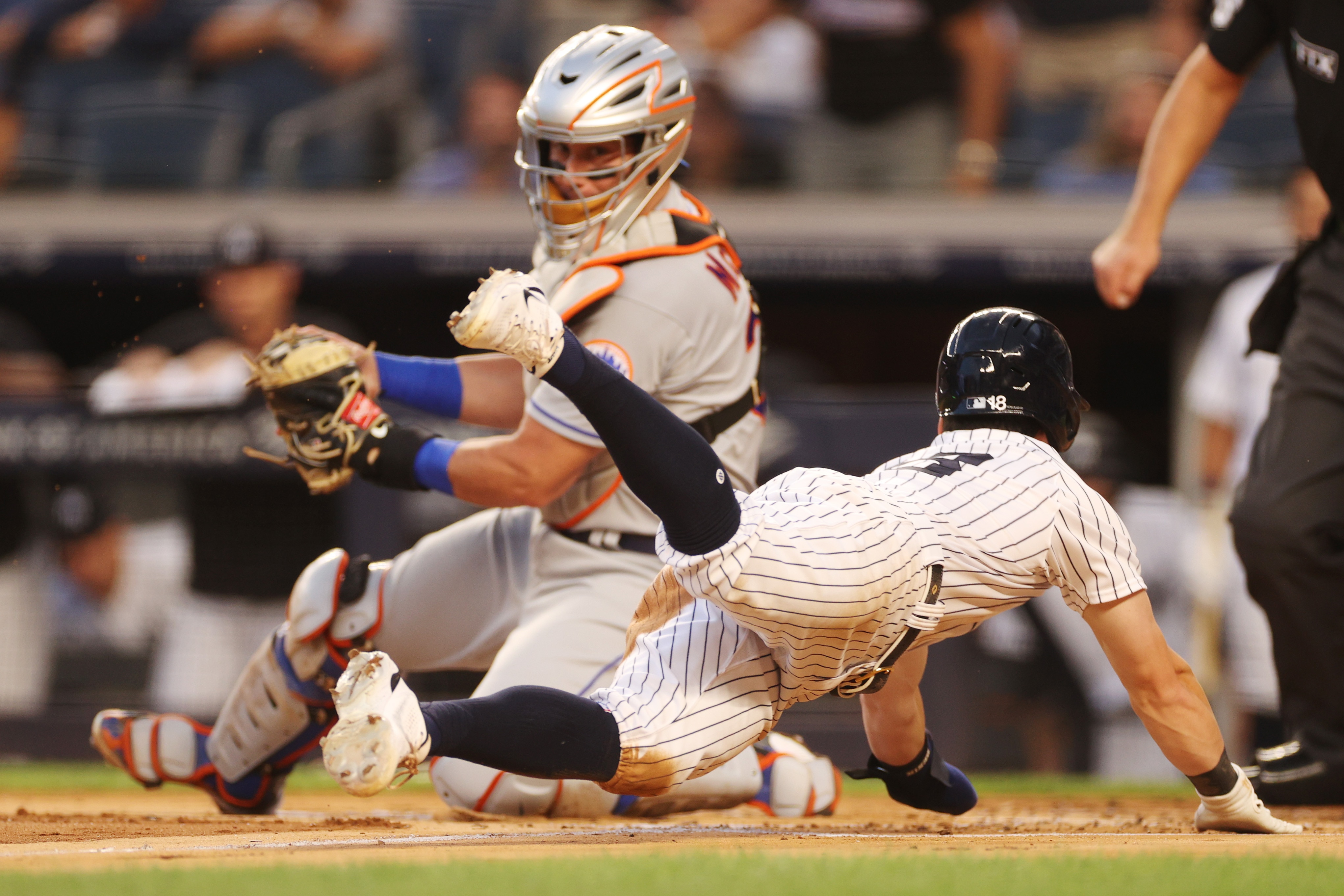 NEW YORK, NEW YORK - AUGUST 22: Andrew Benintendi #18 of the New York Yankees slides safely into home ahead of the tag by James McCann #33 of the New York Mets on a sacrifice fly hit by DJ LeMahieu #26 of the New York Yankees during the first inning at Yankee Stadium on August 22, 2022 in the Bronx borough of New York City.