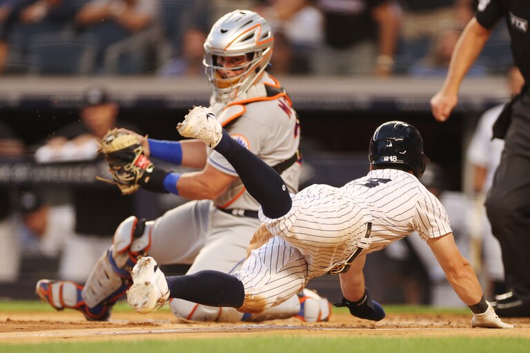 NEW YORK, NEW YORK - AUGUST 22: Andrew Benintendi #18 of the New York Yankees slides safely into home ahead of the tag by James McCann #33 of the New York Mets on a sacrifice fly hit by DJ LeMahieu #26 of the New York Yankees during the first inning at Yankee Stadium on August 22, 2022 in the Bronx borough of New York City.