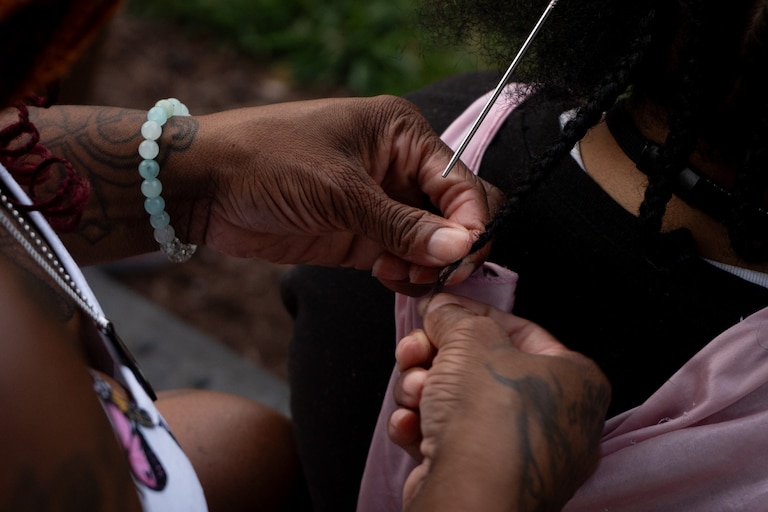 Hair braider, Crystal, braids a clients hair outside of the Baltimore Visitor Center hair as the two wait for the fireworks and drone display on July 4, 2024.