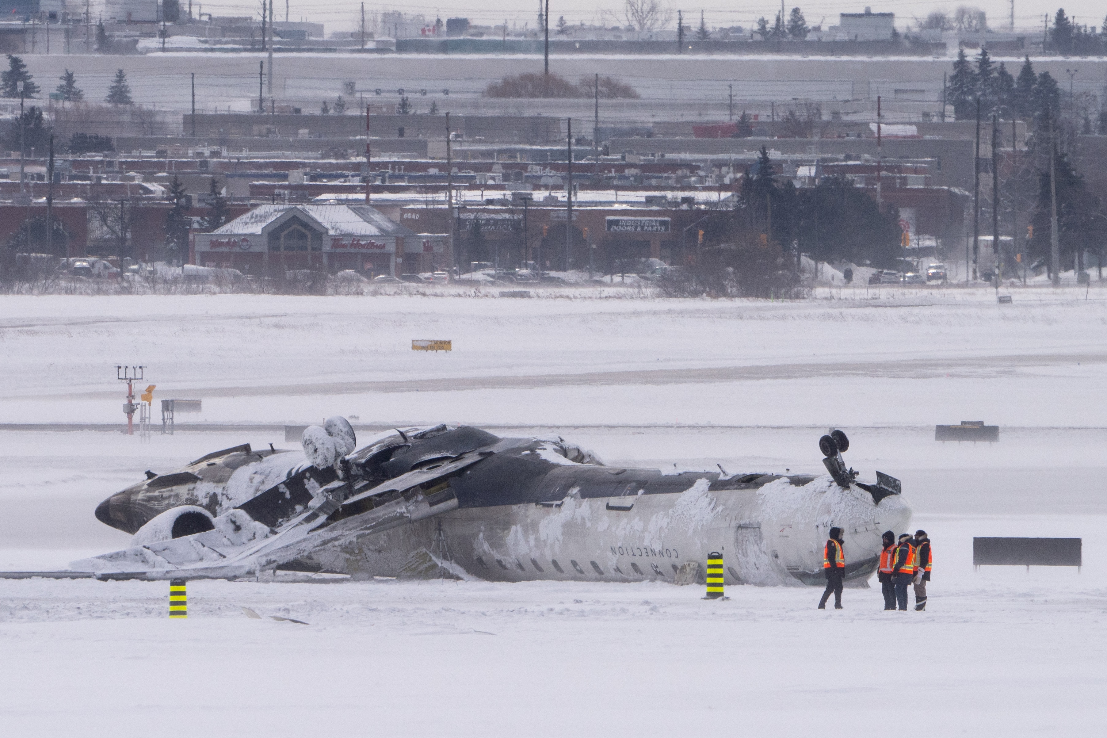 TORONTO, CANADA - FEBRUARY 18: Airport workers survey the site of a Delta Air Lines plane crash that injured at least 18 passengers at Toronto Pearson International Airport on February 18, 2025 in Toronto, Canada. The jet, coming in from Minneapolis, attempted to land amid strong winds and snow, leading to it crashing and landing upside down on the tarmac the day before. (Photo by Katherine KY Cheng/Getty Images)
