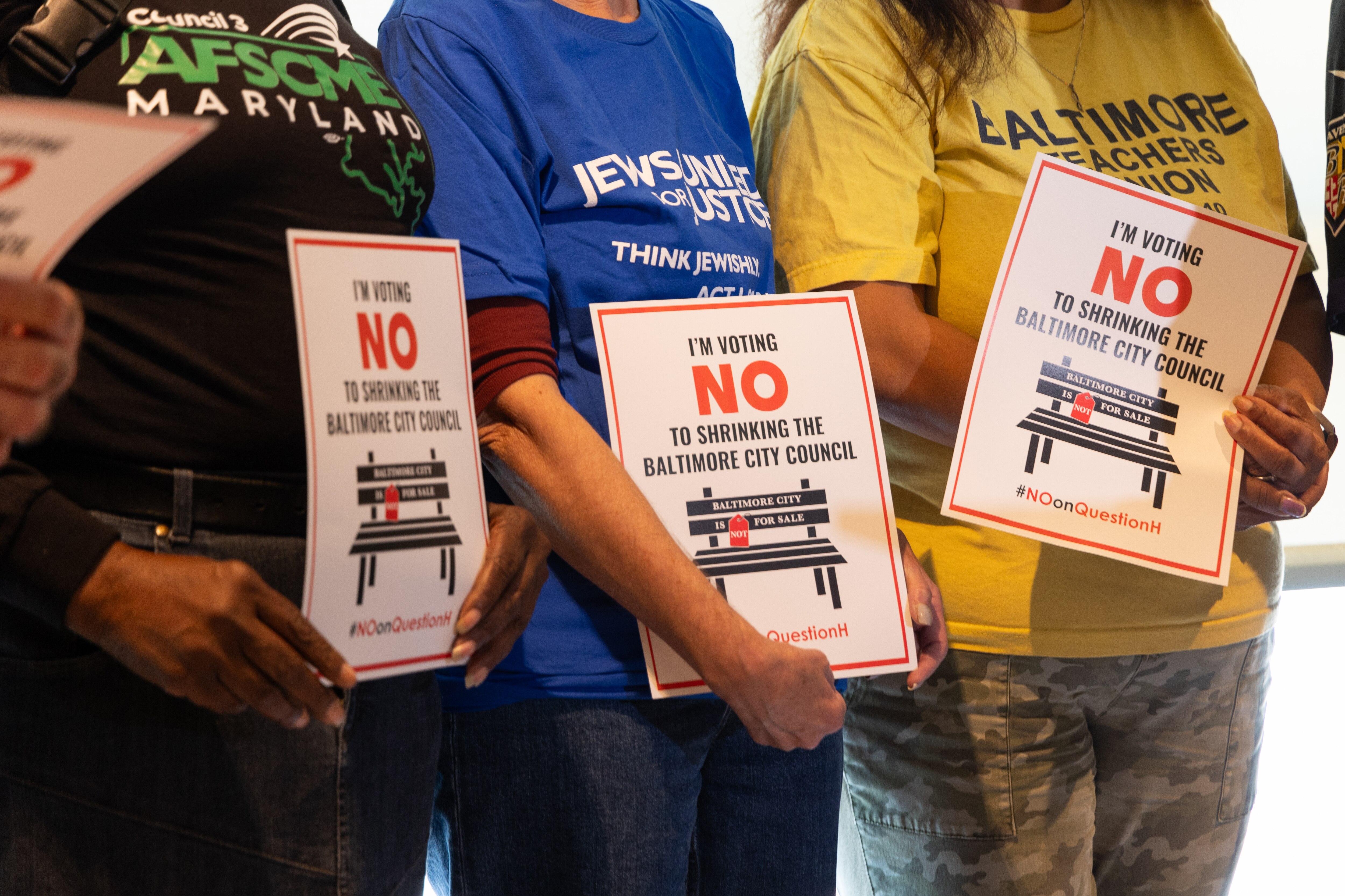 Spectators hold signs opposing the bill that would reduce the size of City Council during a press conference in Zeke’s Coffee Shop on September 15, 2024.
