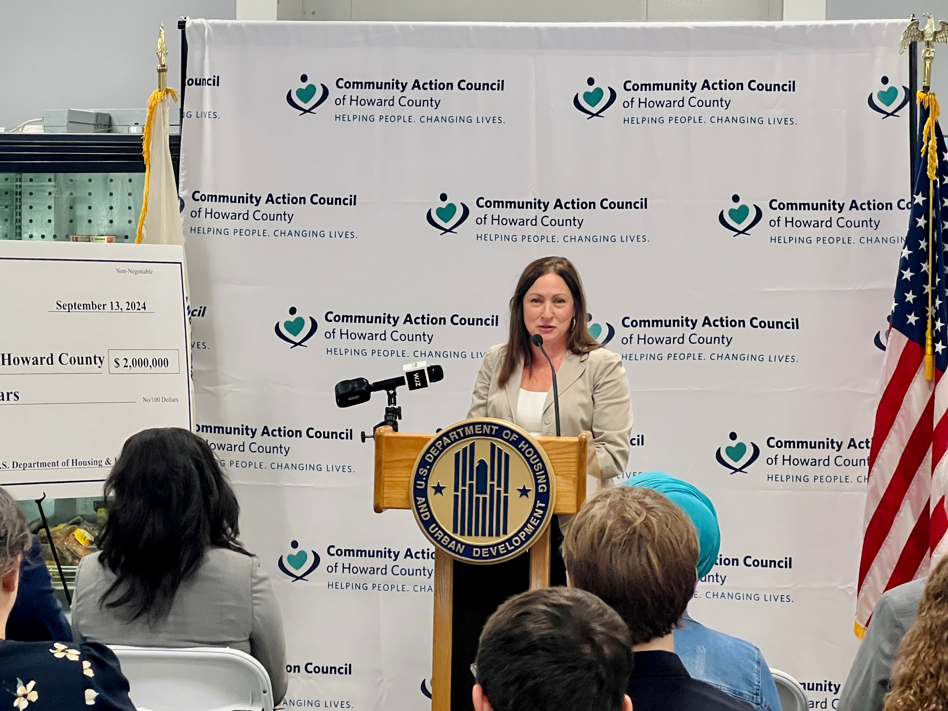 A woman stands at a podium at a press conference and speaks to a crowd.