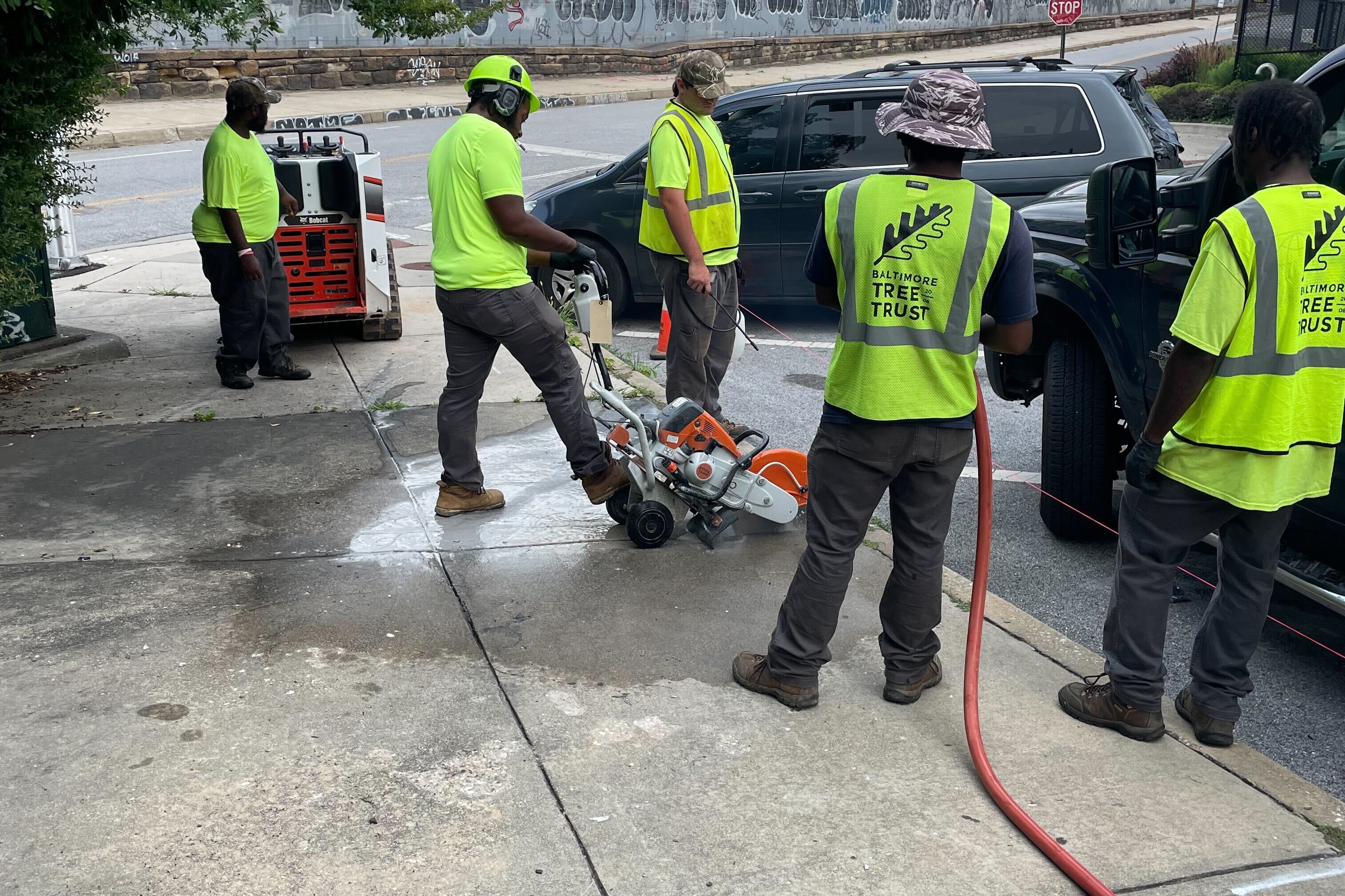 A crew works to cut out a piece of the sidewalk to be replaced with a tree well.