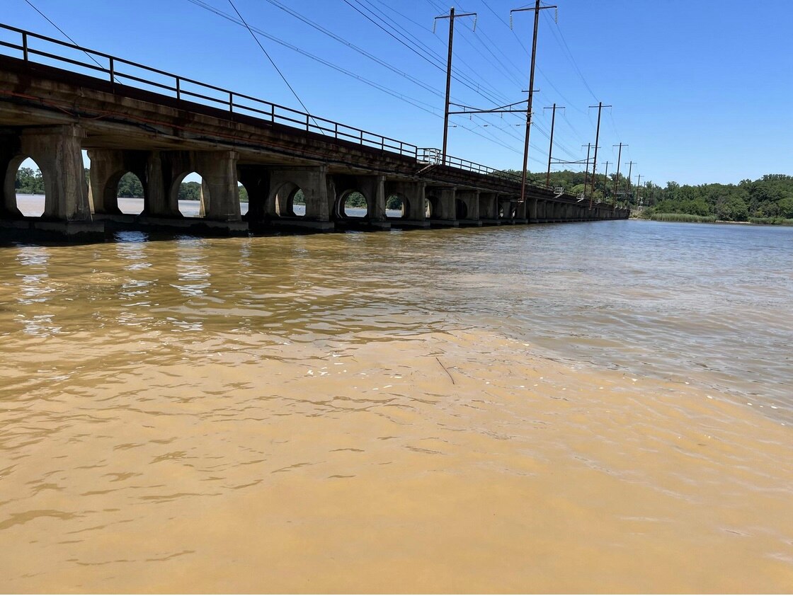 A railroad bridge crosses over brown, cloudy water in the Gunpowder River.