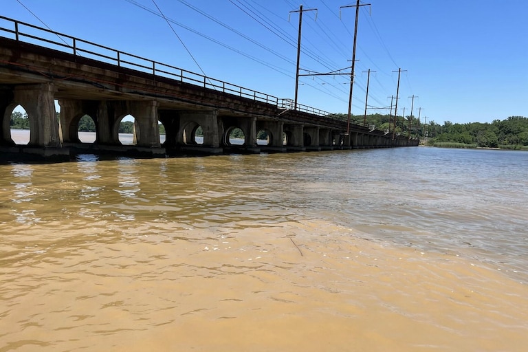 A railroad bridge crosses over brown, cloudy water in the Gunpowder River.