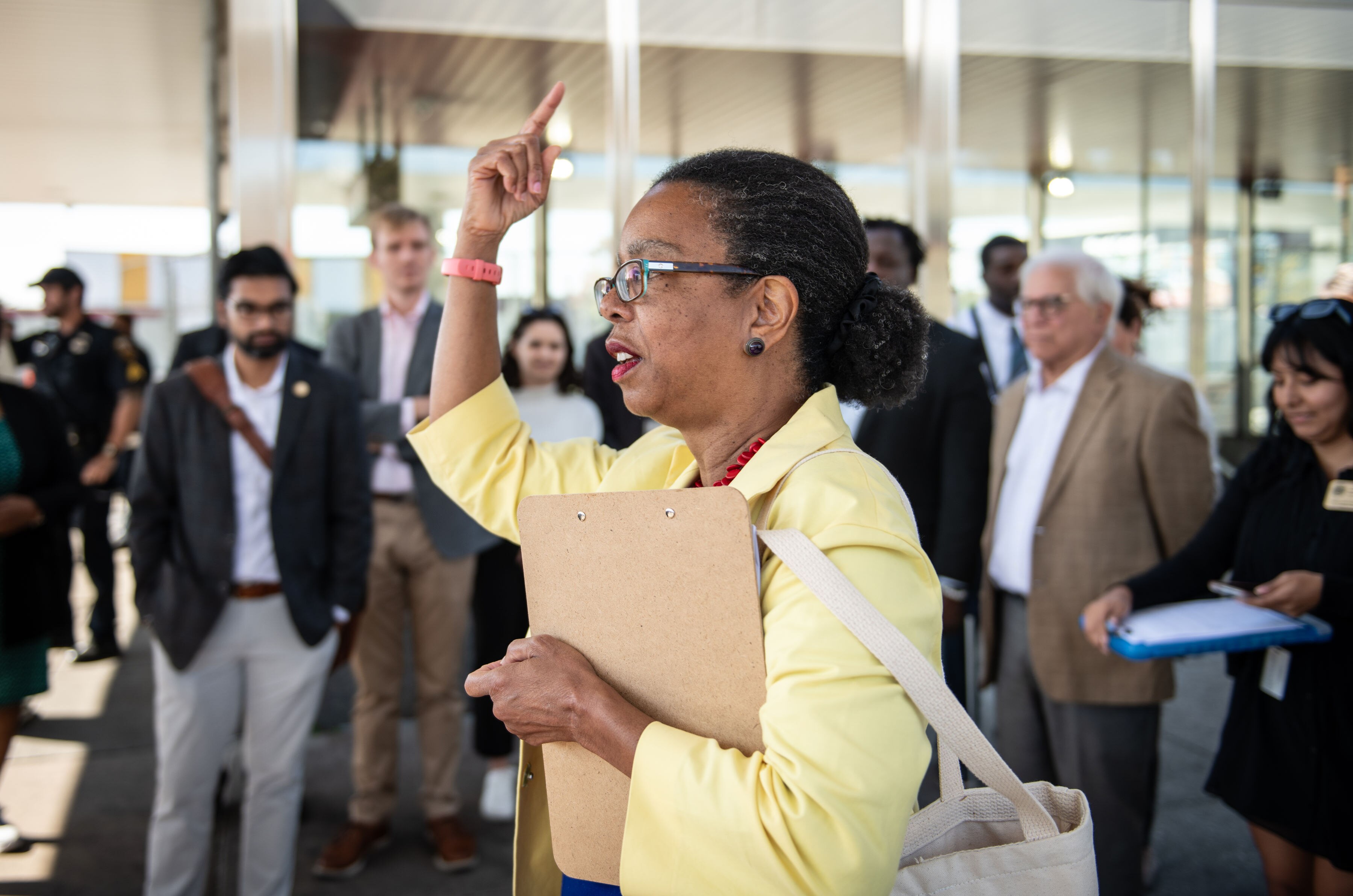 State delegate Robbyn Lewis, wearing a yellow jacket and raising her right hand, addresses a small crowd of people.