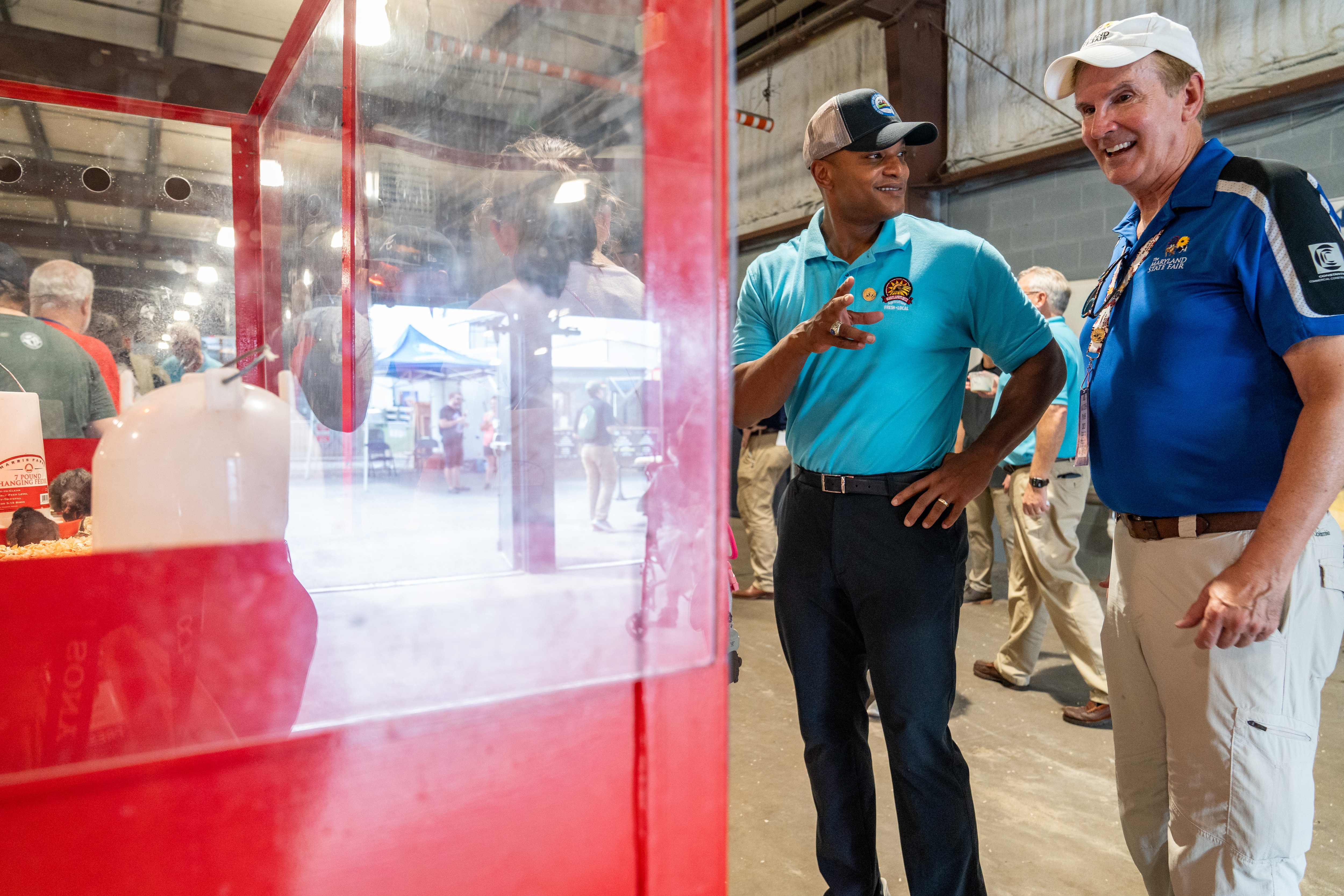 Gov. Wes Moore and Gerry Brewster share a laugh as they stand near a red enclosure housing chicks that are about three days old.