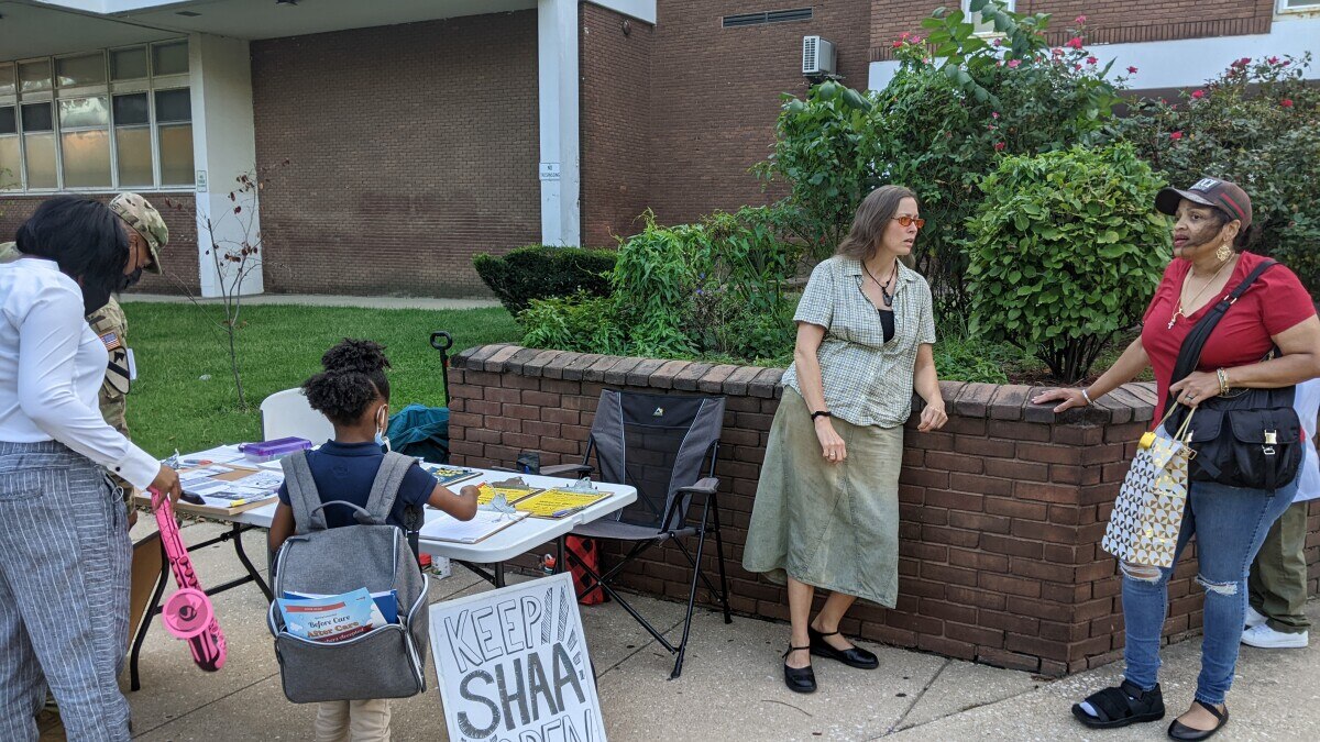 Members of the Steuart Academic Academy community gather around a table. Forms and documents about efforts to keep the school open are spread across the table.