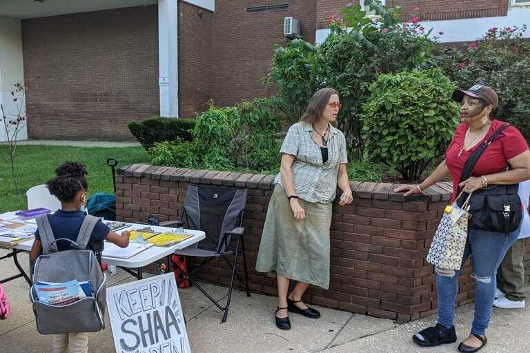 Members of the Steuart Academic Academy community gather around a table. Forms and documents about efforts to keep the school open are spread across the table.